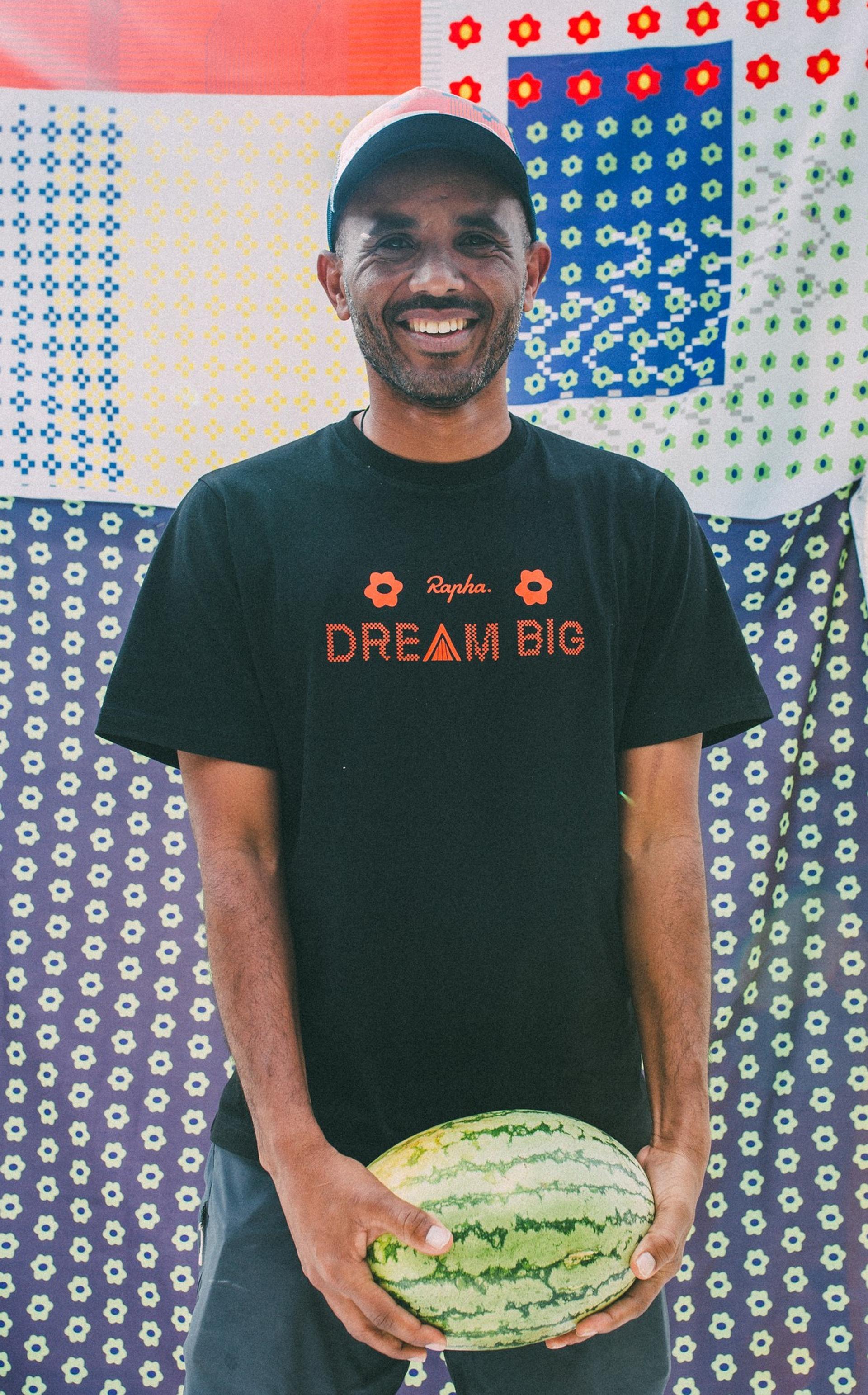 Smiling man holding a cut watermelon in front of colorful patterned wall decorations