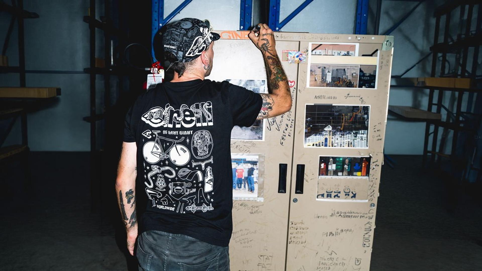 Mike Giant, wearing a Cinelli T-shirt, works on tattoo-flash artwork at a computer in a studio.