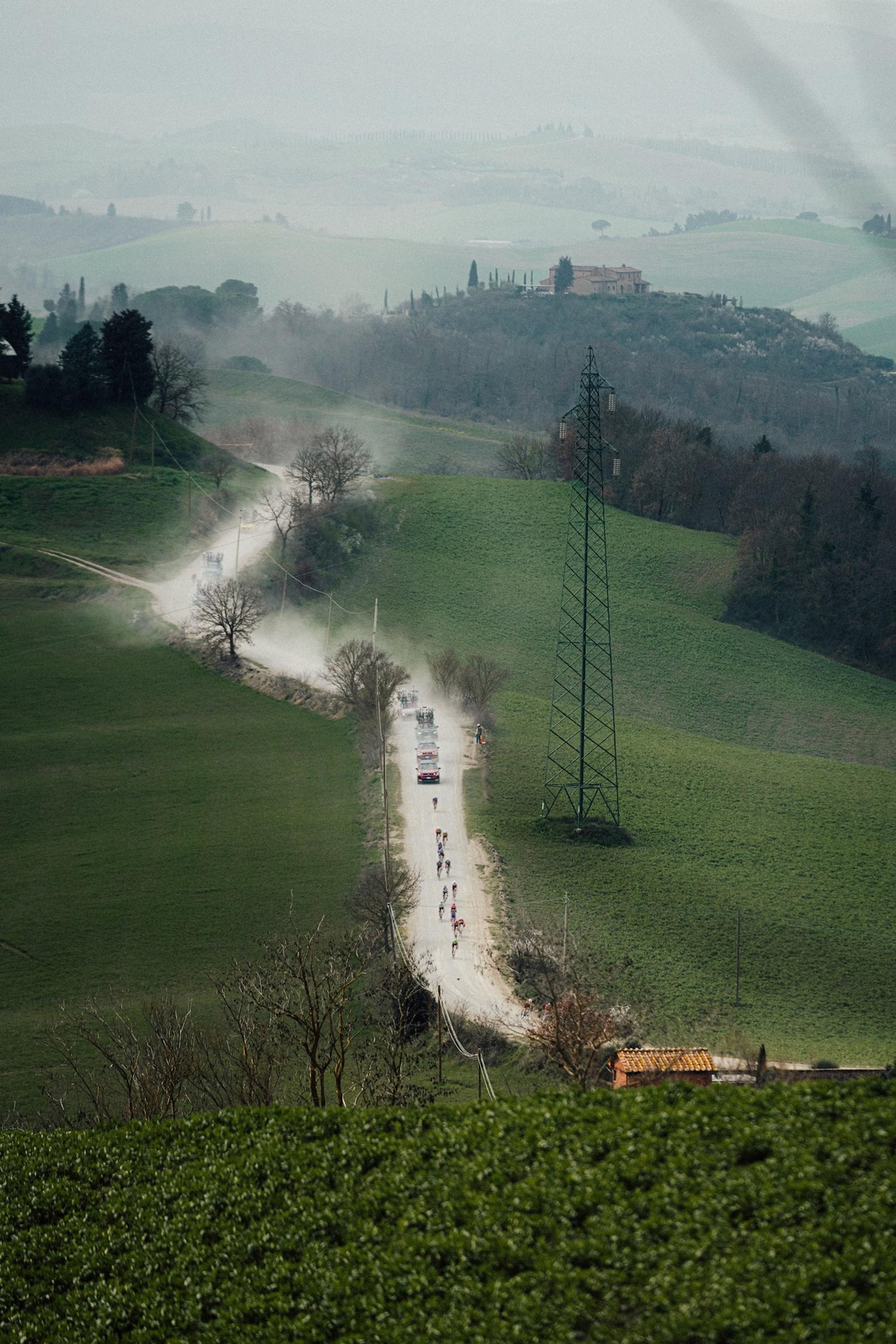 Peloton and team cars kick up dust on the white gravel roads of the Women Elite Strade Bianche in Tuscany, Italy.