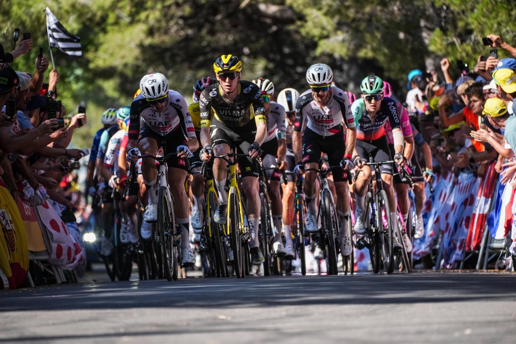 Cycling peloton rides close together under colorful crowd at the roadside race finish stretch.