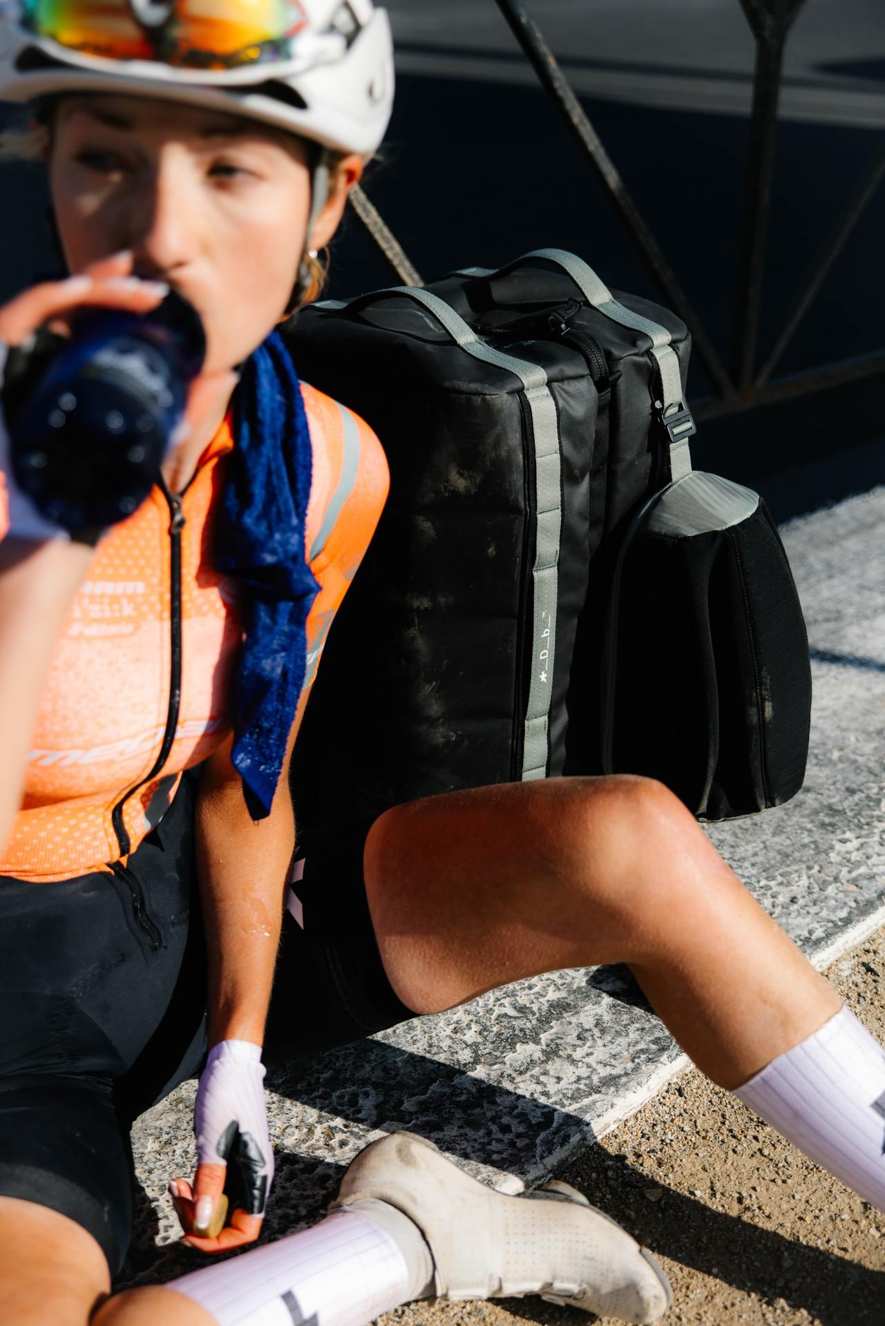 Athlete kneels in white socks and gloves while packing black sports gear on a street curb