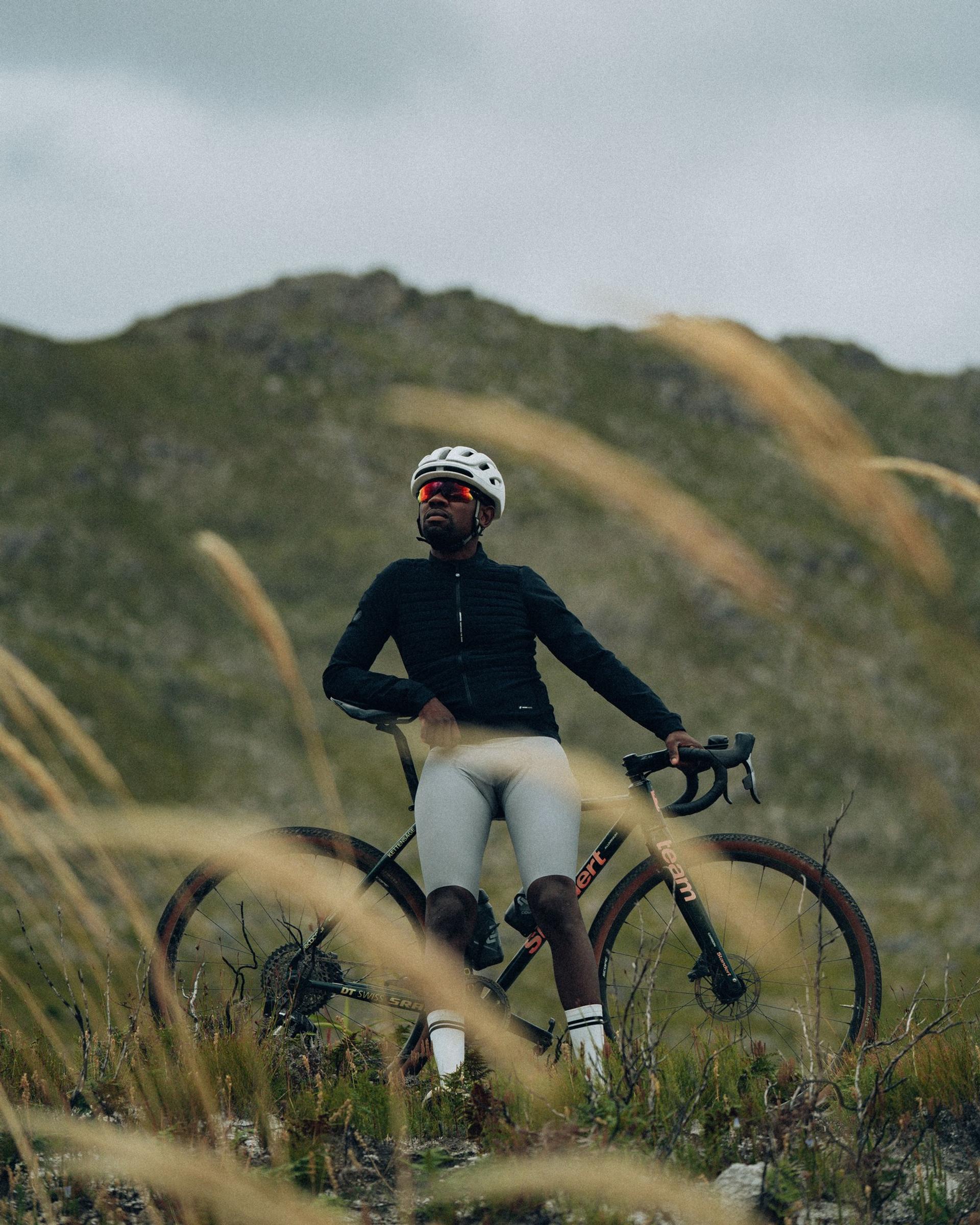 Cyclist in helmet and black kit rides a mountain road bike through grass beside hills