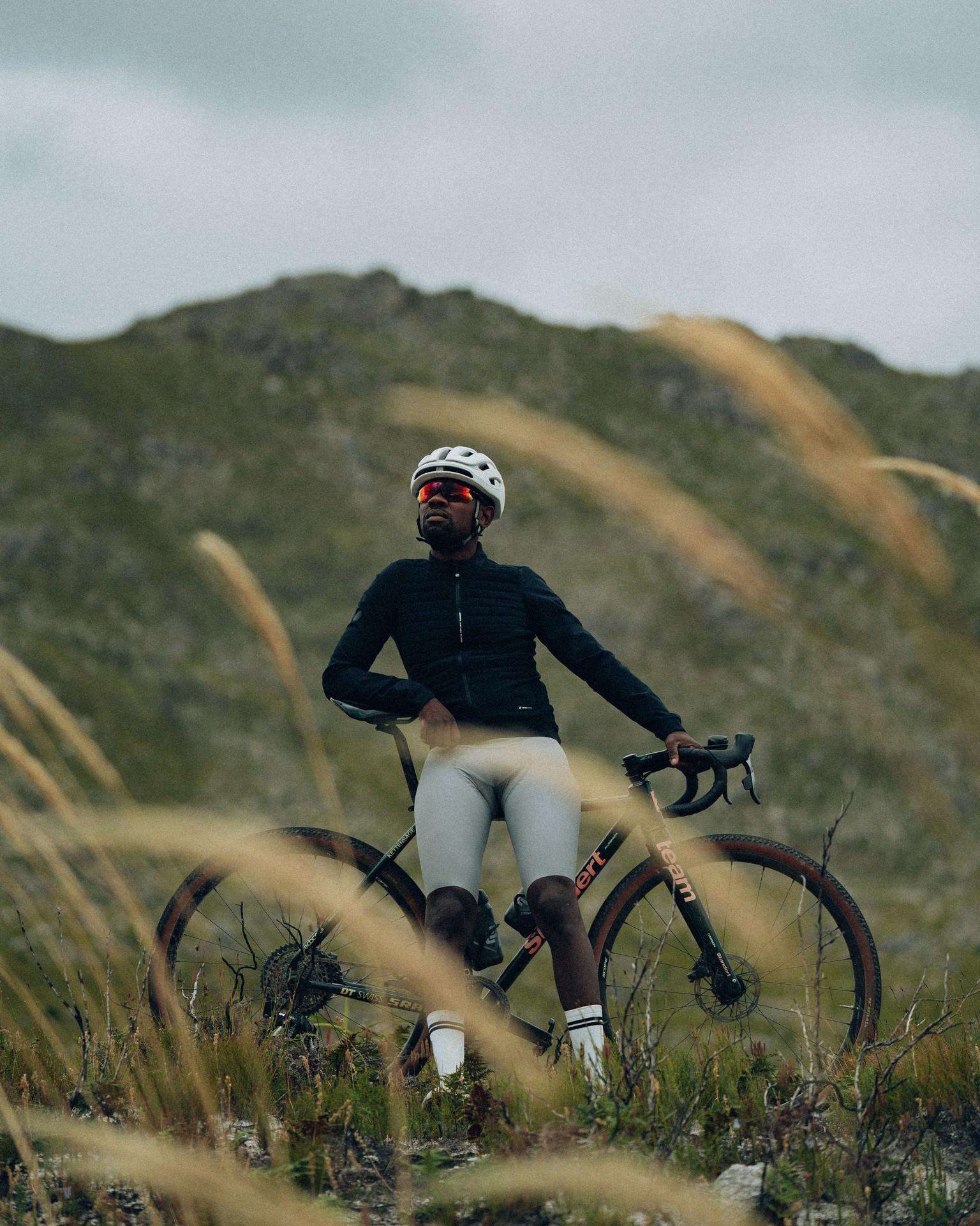 Cyclist in helmet and black kit rides a mountain road bike through grass beside hills