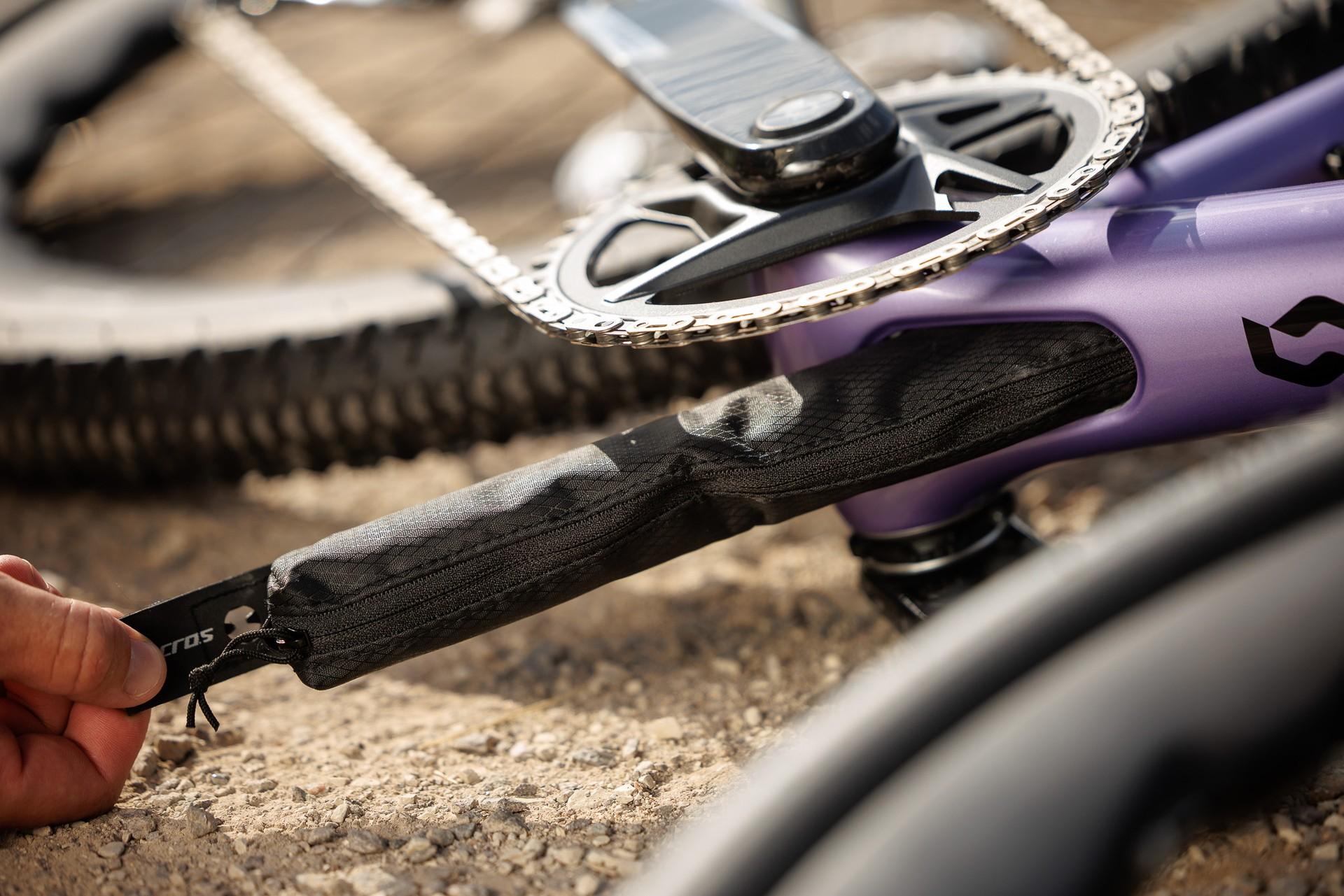 Close-up of a purple Scott gravel bike’s crankset, chain and textured chainstay protector, with a hand holding the frame.