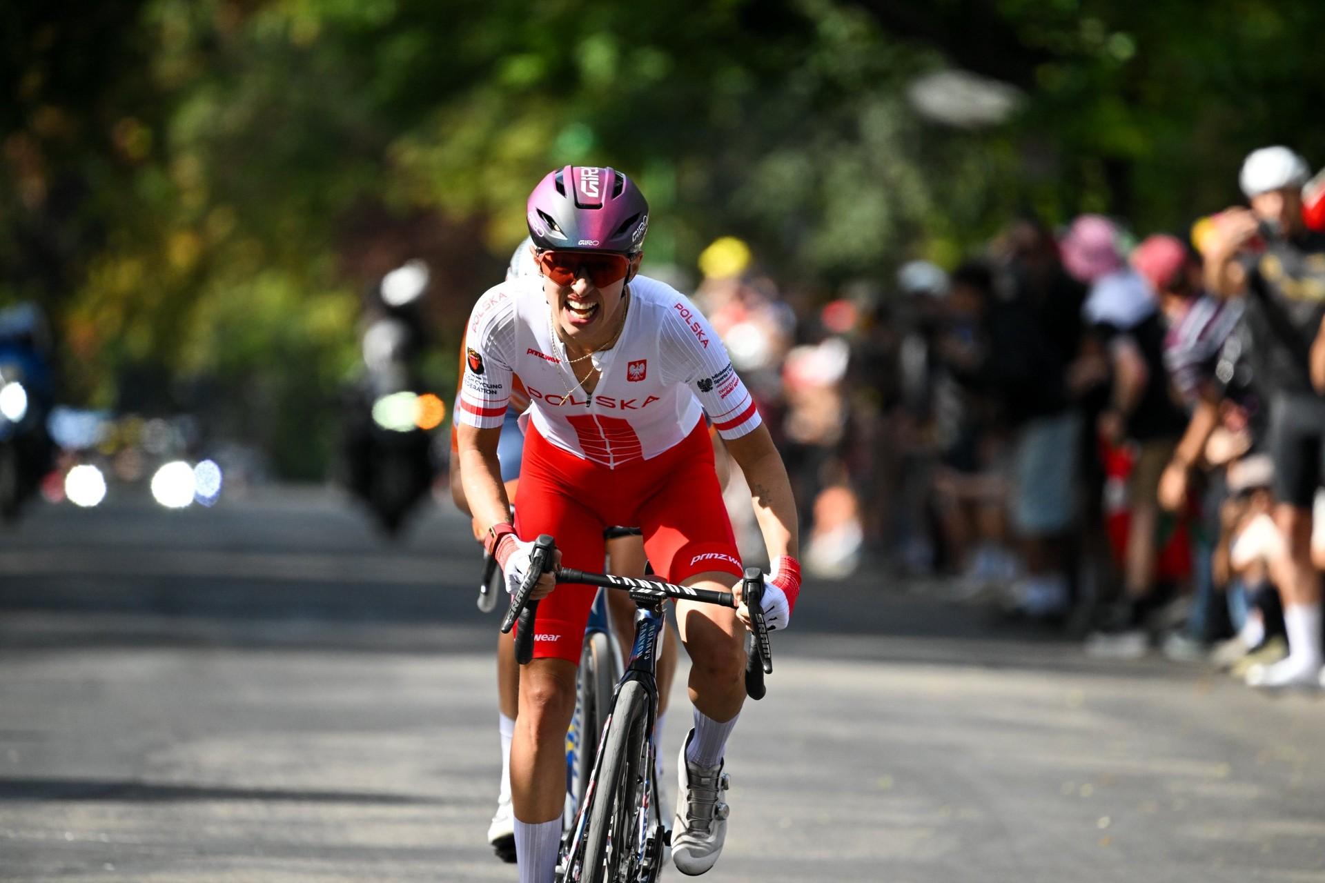 Demi Vollering rides at the front of a European road race, wearing a pink helmet and white jersey.