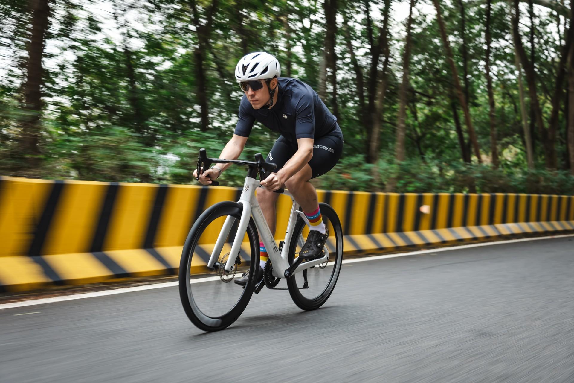 Cyclist in a time-trial position rides a road bike during a race on a tree-lined highway.