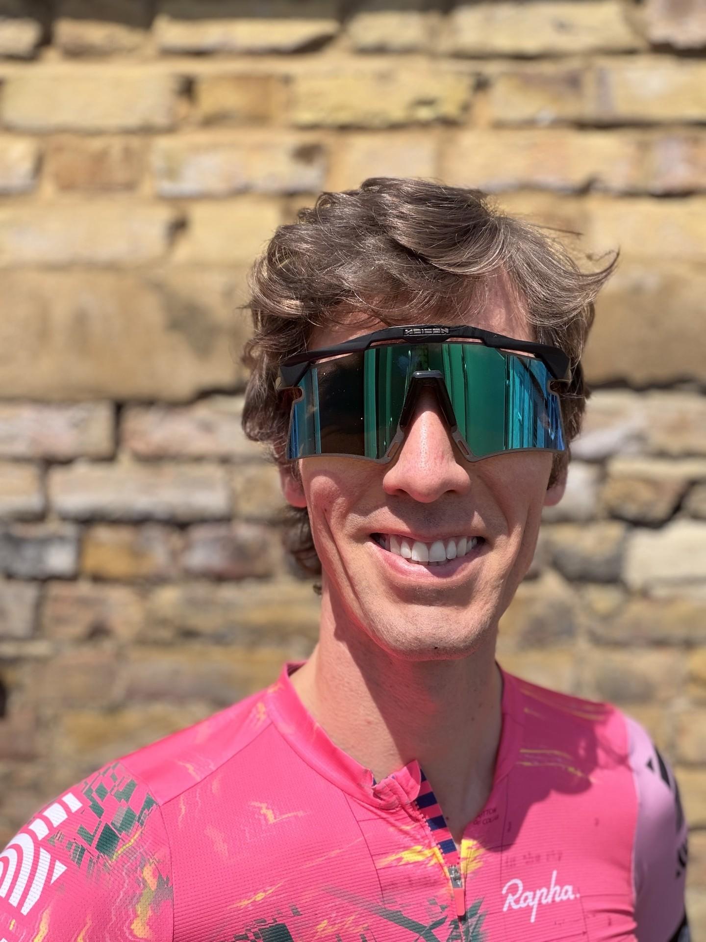 Cyclist in pink Rapha jersey standing outdoors against a stone wall backdrop