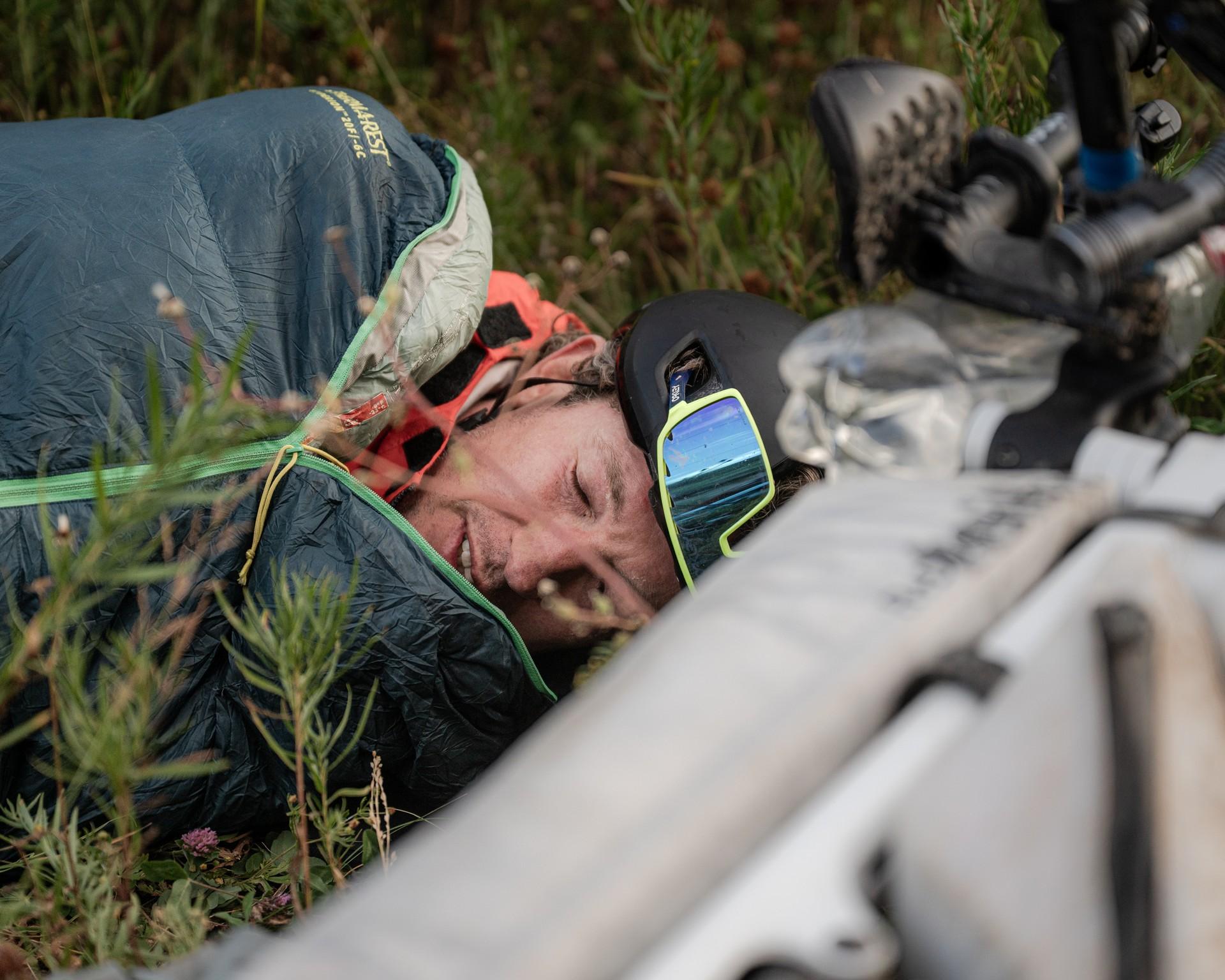 Justinas Leveika lies exhausted beside his bike in the grass, still wearing his helmet.