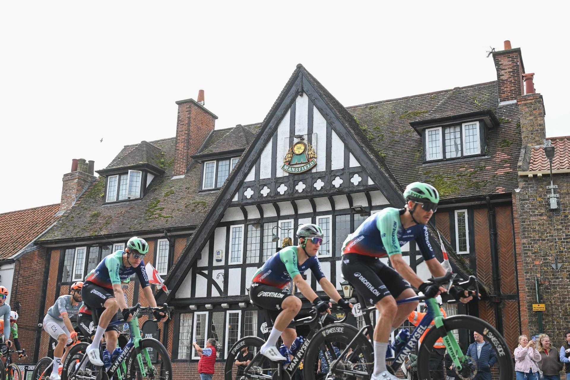Émilien Jacquelin and teammates race past a Tudor-style building during the Tour of Britain