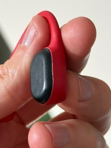 Hand holding a red AfterShokz Aeropex headset with casing separated from the black bone-conduction unit