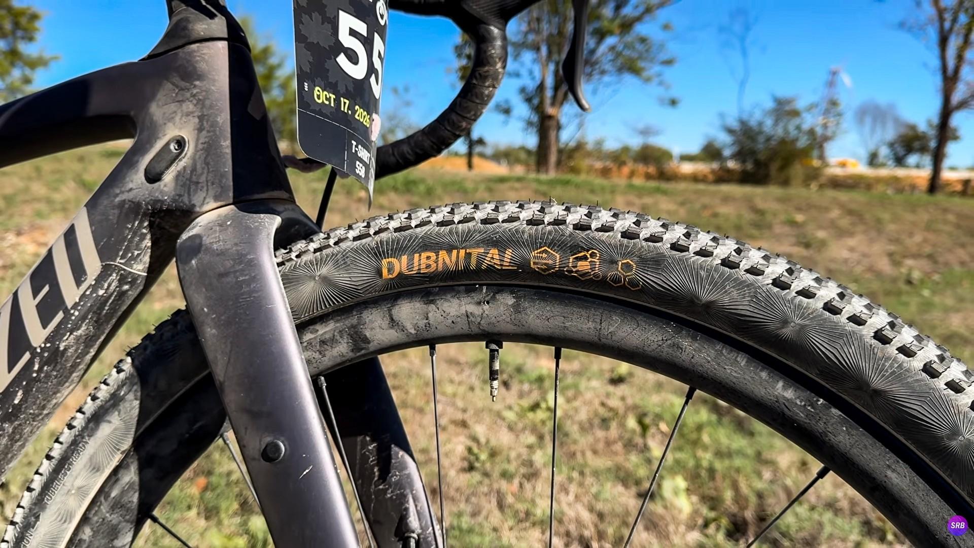 Close-up of a gravel bike’s front wheel, fork and race number on a dry course