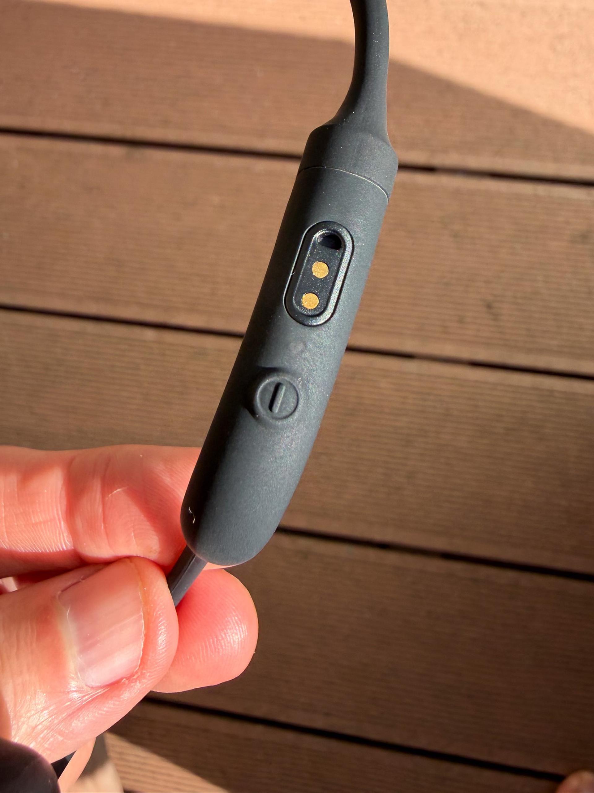 A hand holds the Philips open-ear headphones, showing a control button and yellow indicator against wooden decking.