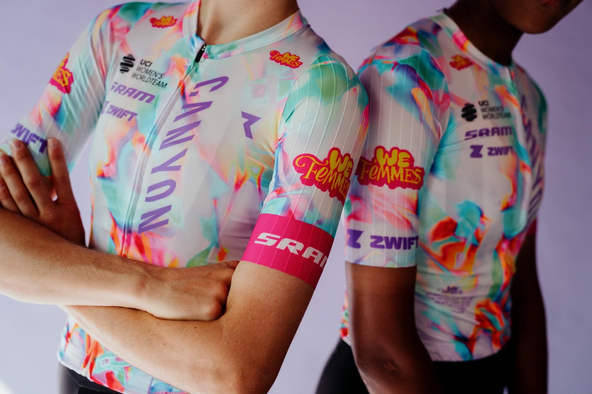 Cycling team members in colorful performance jerseys pose with arms crossed at an event