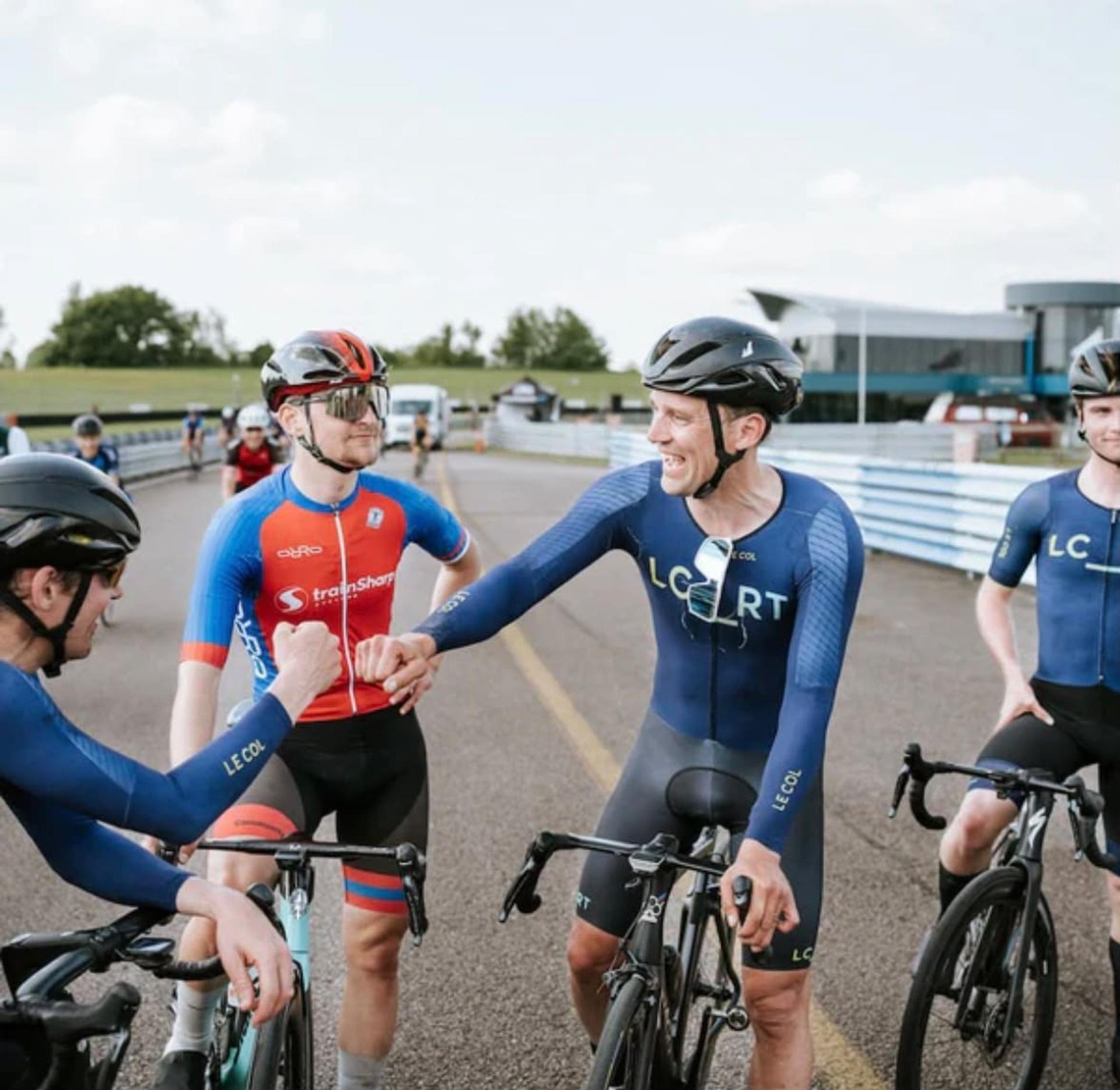 Cyclists in blue kits greet and shake hands with their team on a trackside road.