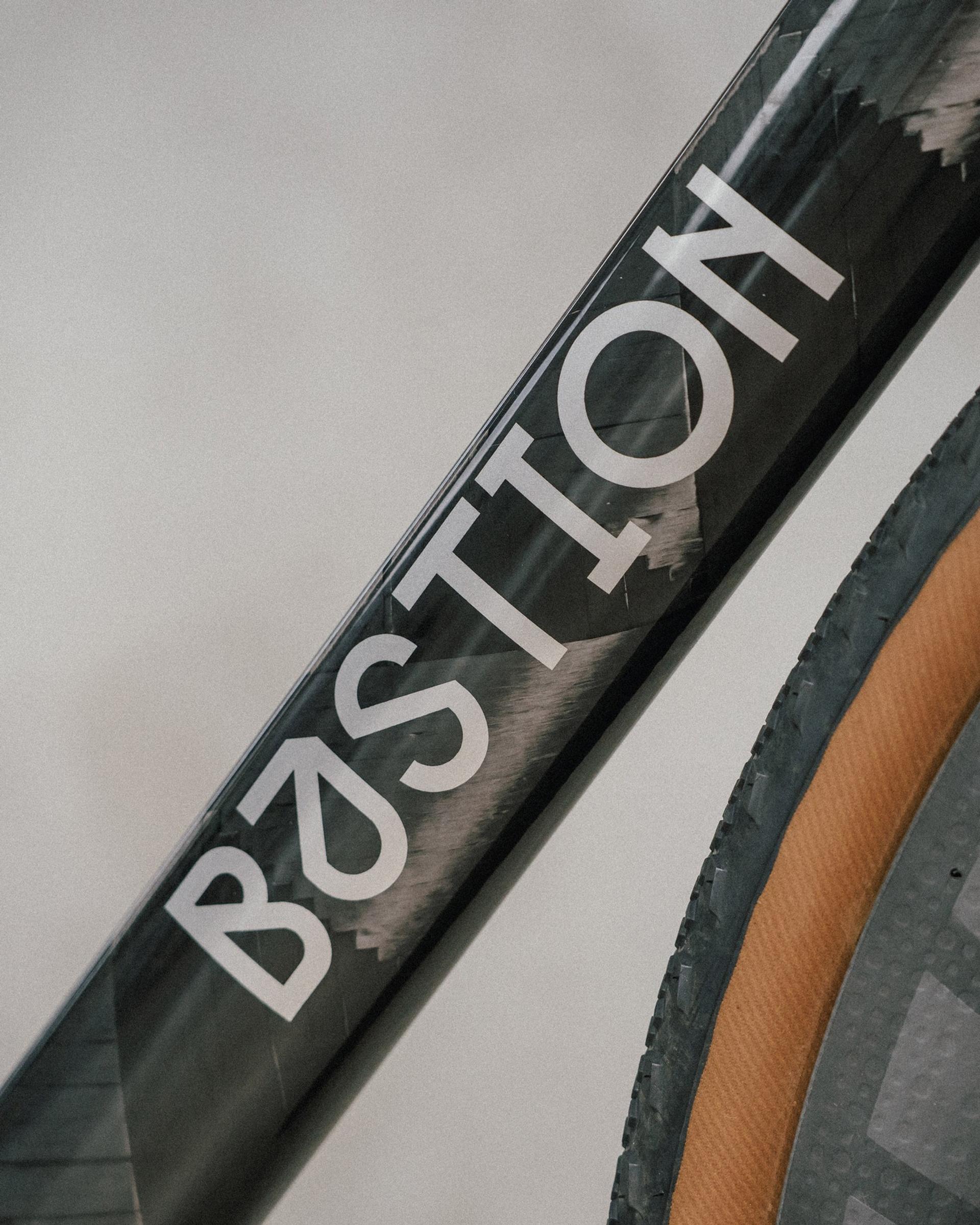 Close-up of BASTION bike frame lettering and a wheel rim against a gray sky