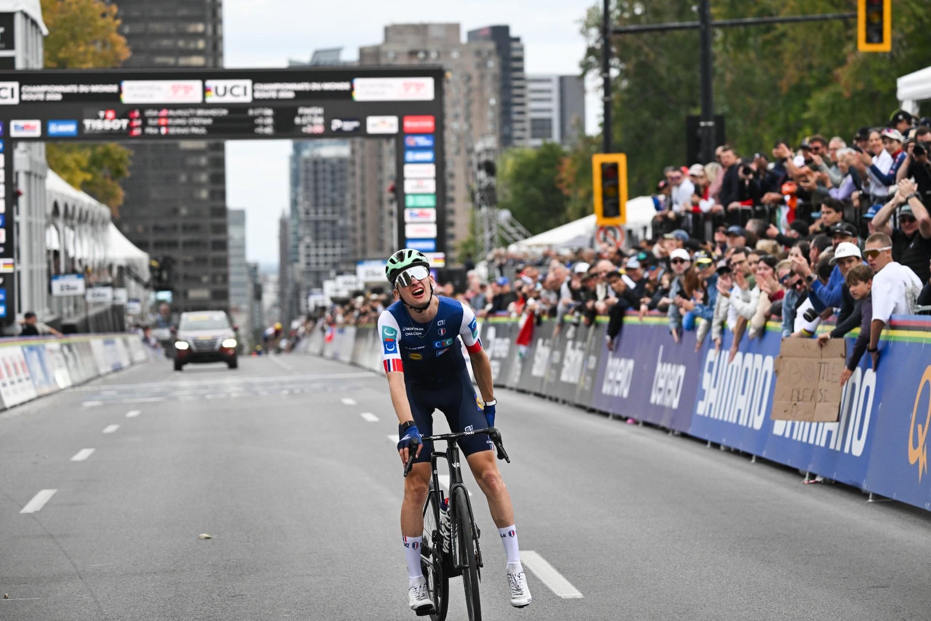 Paul Seixas rides his bike on a city-center course, with spectators cheering behind barriers.