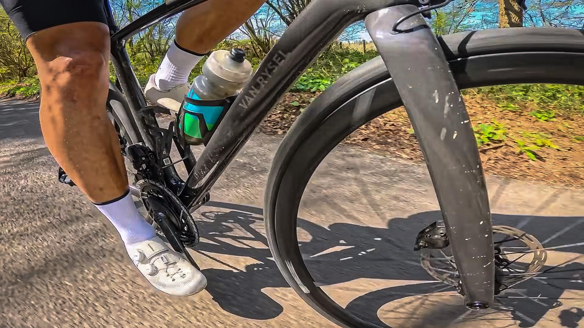 Cyclist in race kit pedals a road bike on a sunny country road, seen from knee and front fork angle