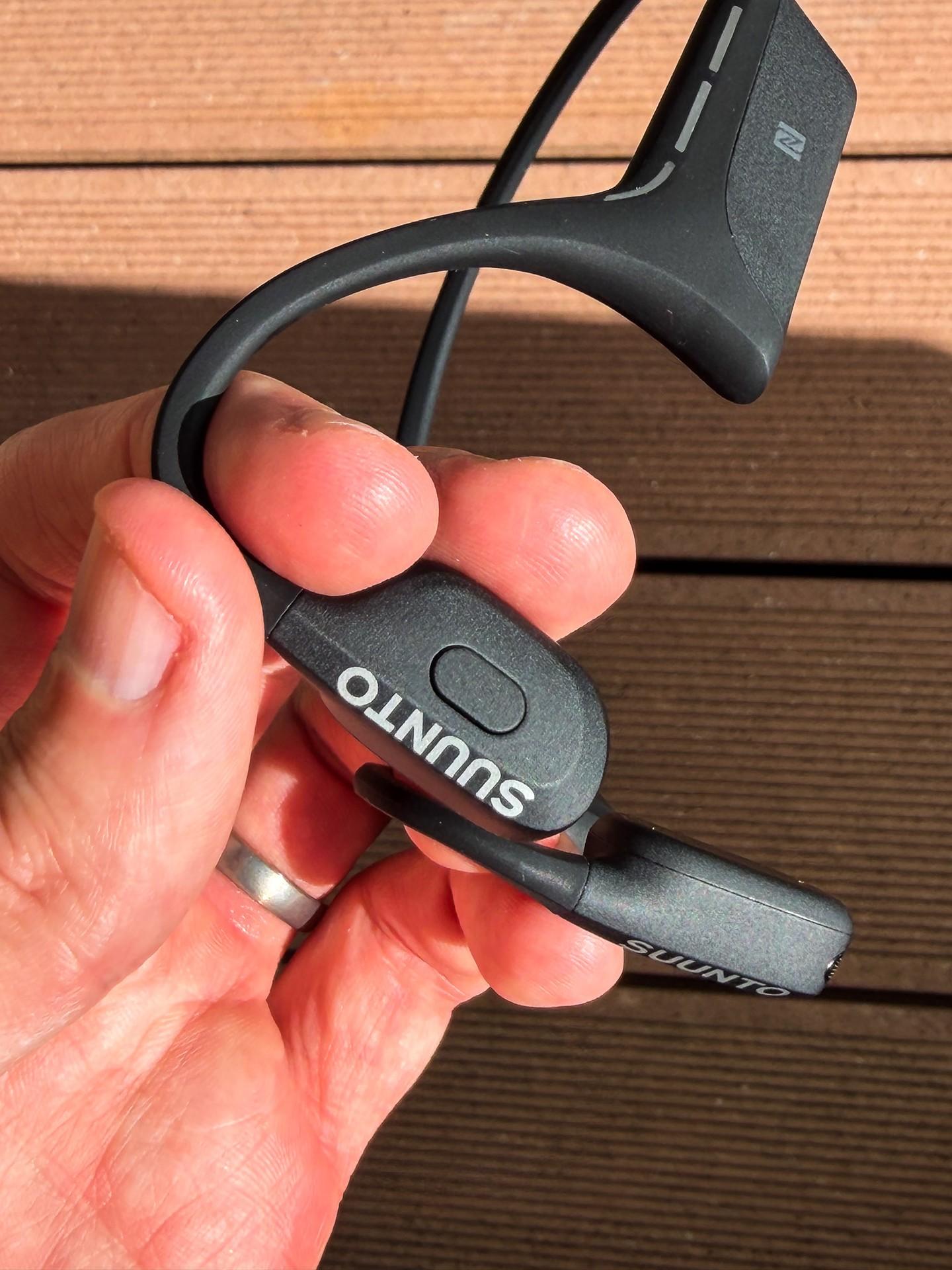 A hand holds the Suunto Wing 2 open-ear headphones, showing the neckband and Suunto-branded control.
