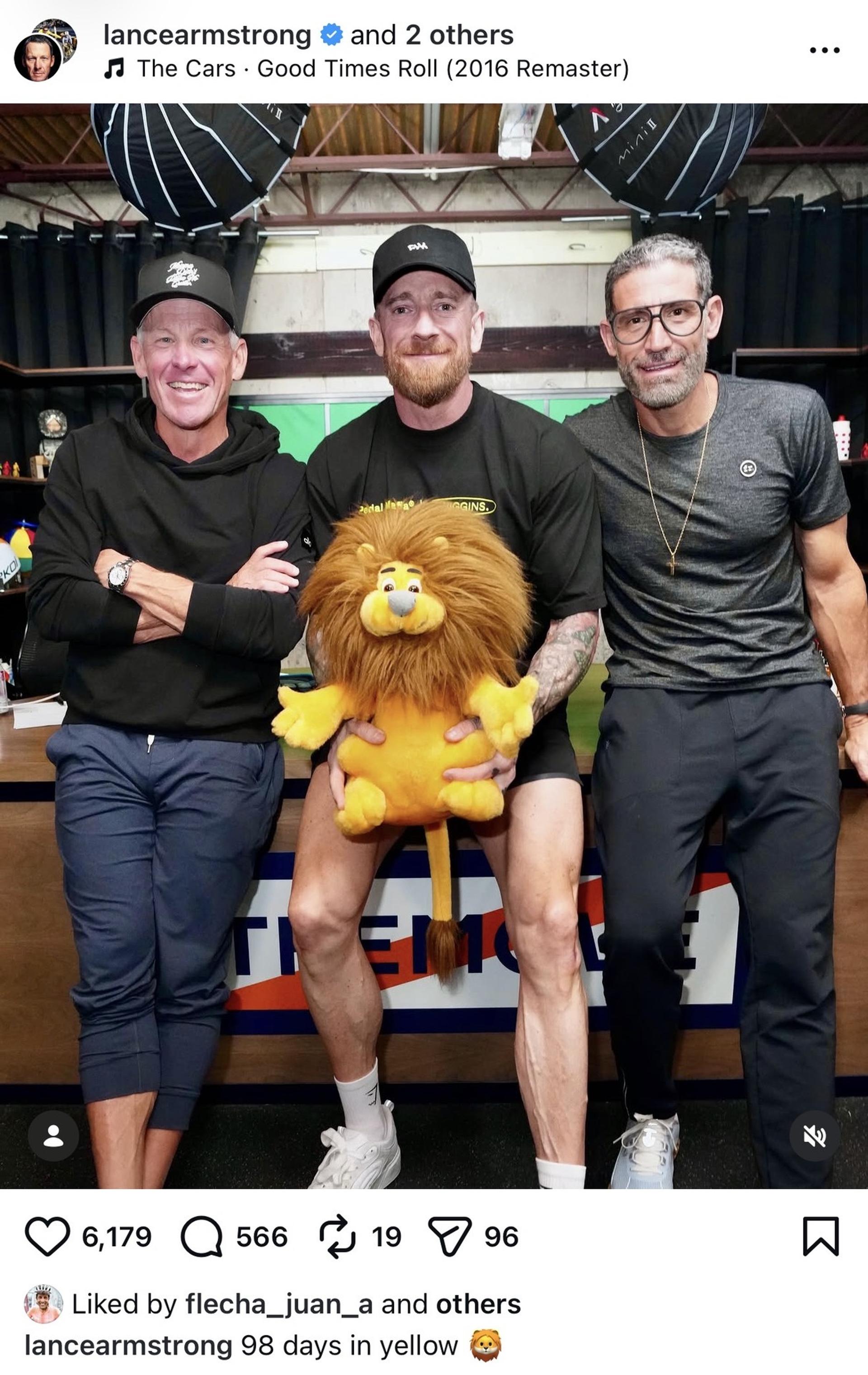 Three men pose with a lion mascot at a cycling event, including Lance Armstrong and two others