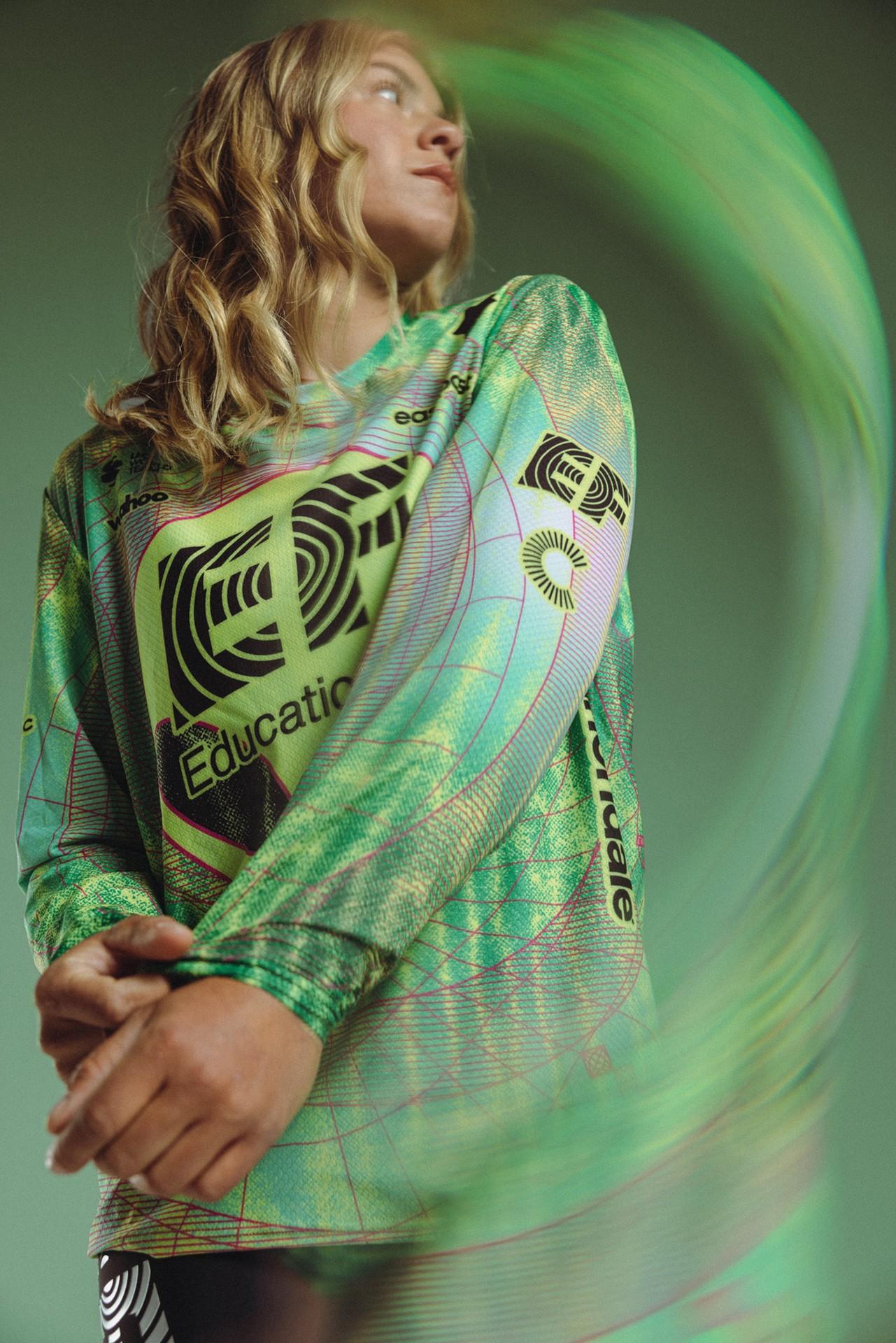 Woman in green-blue hoodie with education logo, posing as colorful spiral light swirls behind her