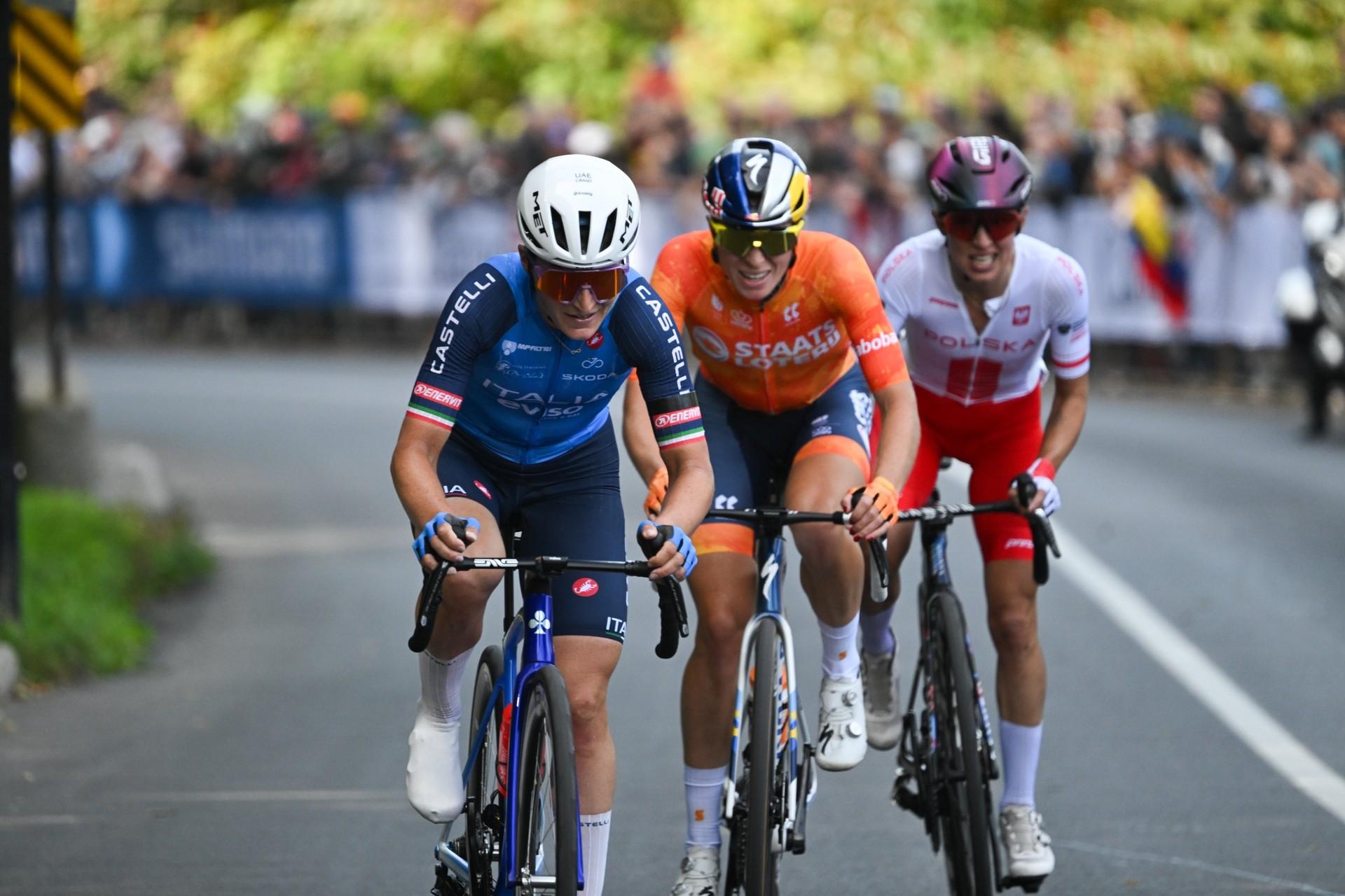 Demi Vollering, wearing the orange Dutch jersey, rides alongside two cyclists in a road race.