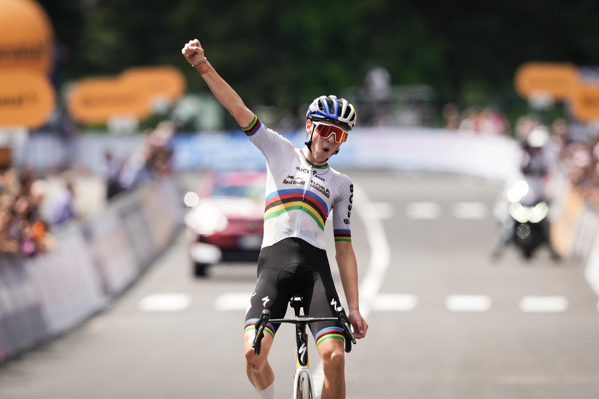 Lorenzo Mark Finn raises a fist while riding his bicycle across the finish line.