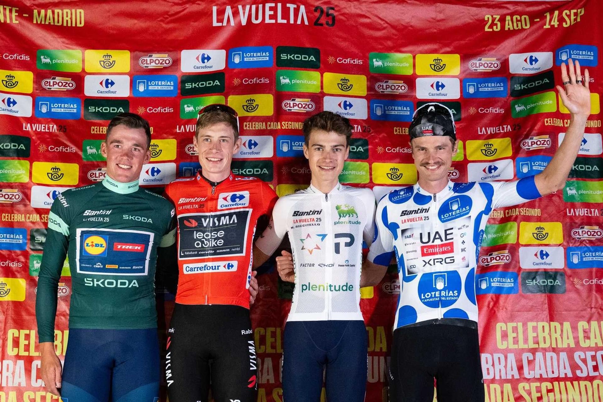 Four Vuelta a España cyclists pose in classification jerseys, with one rider raising his hand.
