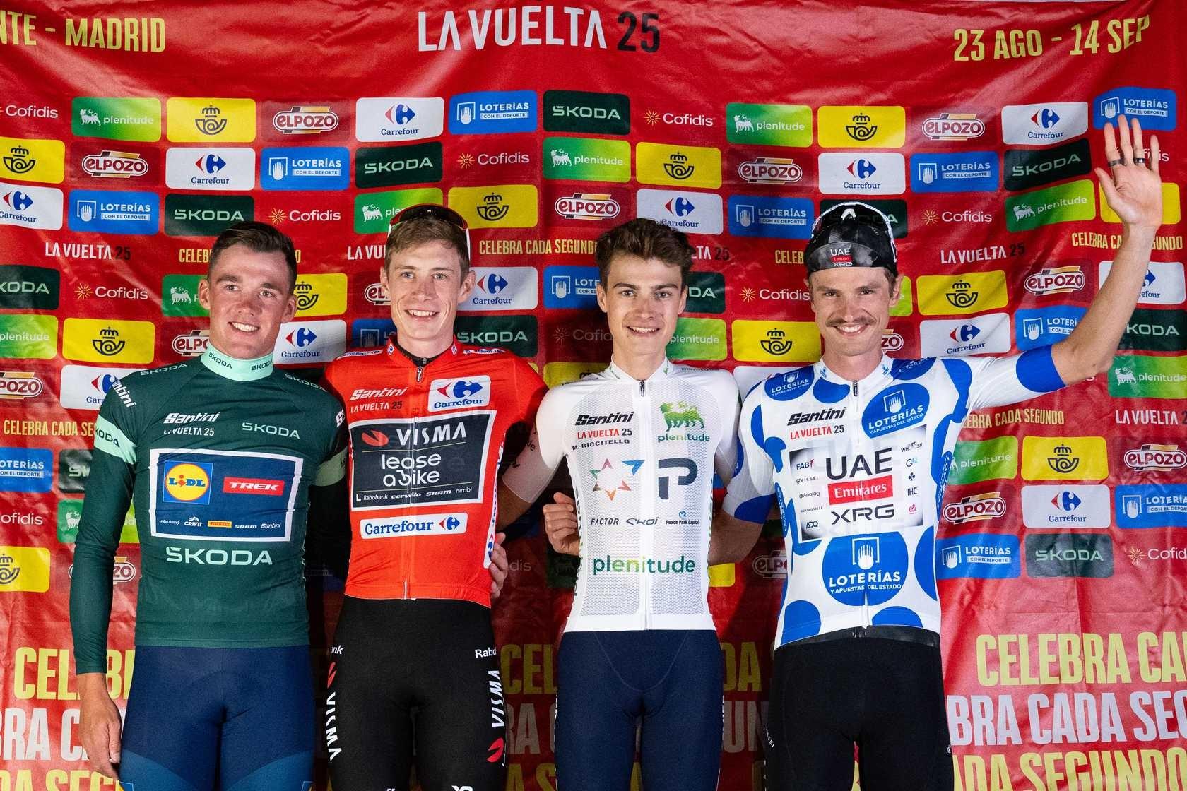 Four Vuelta a España cyclists pose in classification jerseys, with one rider raising his hand.