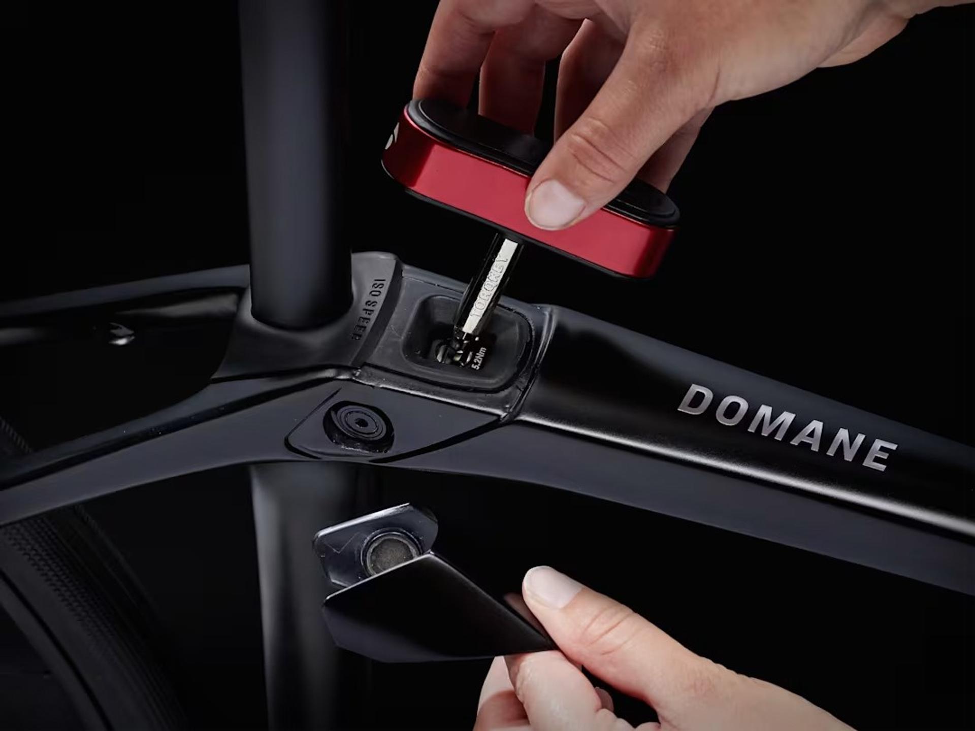 Hands use a red tool to adjust a component on a Domane bicycle frame.