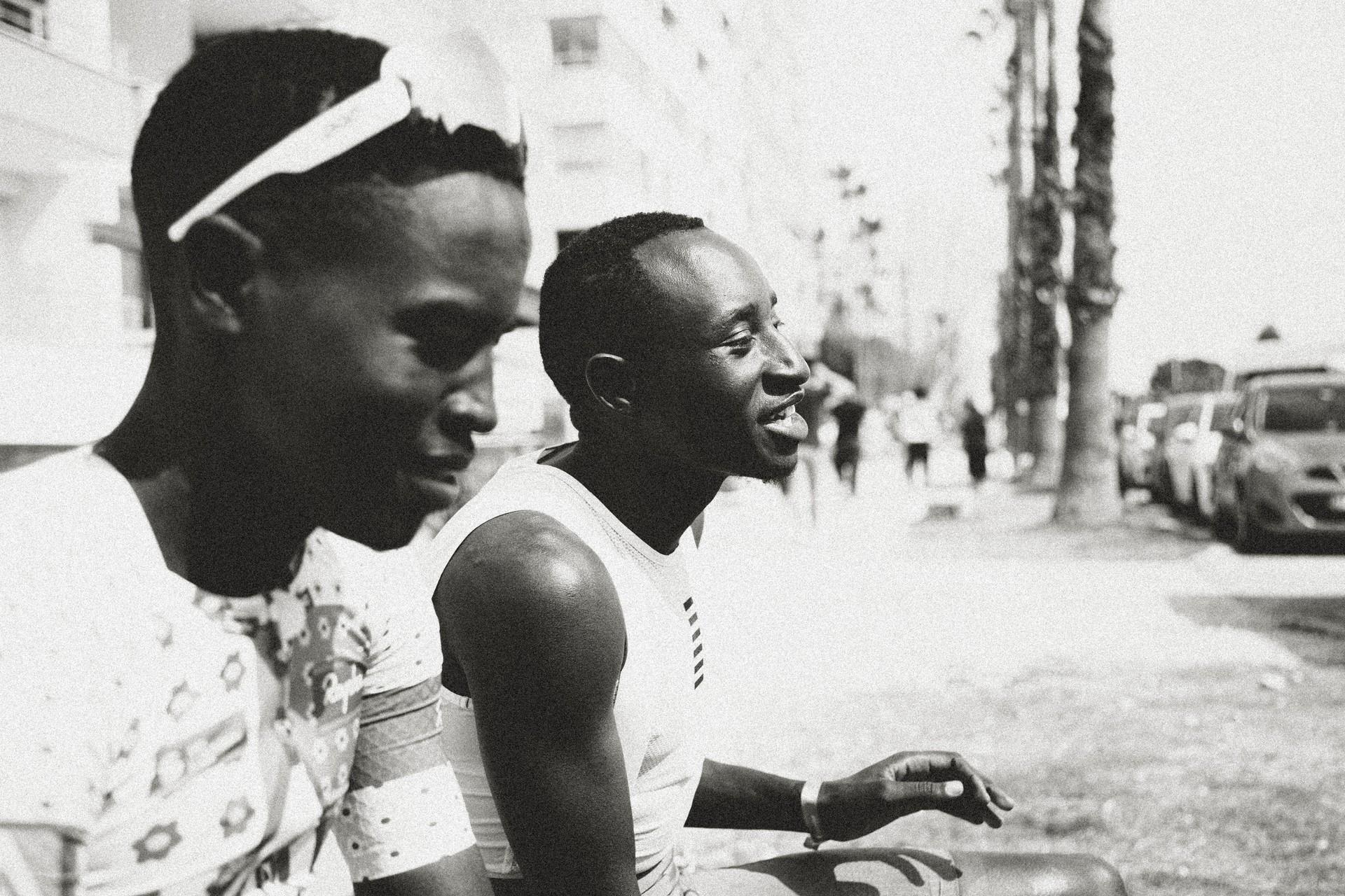 Two young women on a street, one smiling while walking and talking to someone off-camera.
