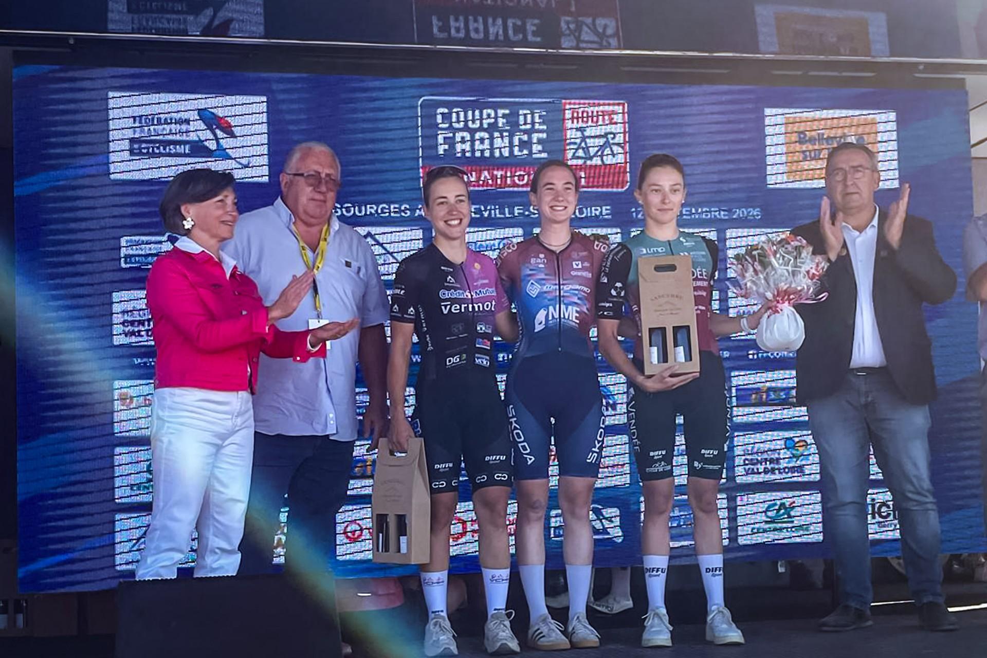 Grace Reynolds and Megamo Vosges teammates celebrate on a podium after Paris-Bourges, holding trophies and flowers.