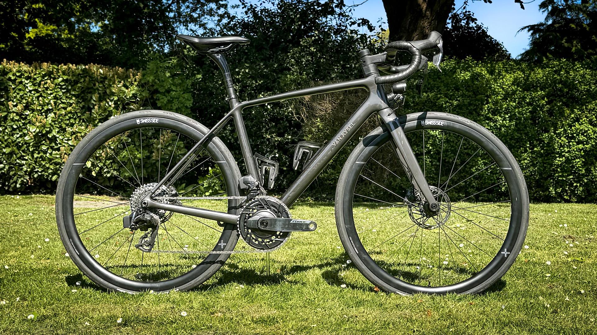 Silver road bike parked on a sunny lawn with trees and hedges in the background