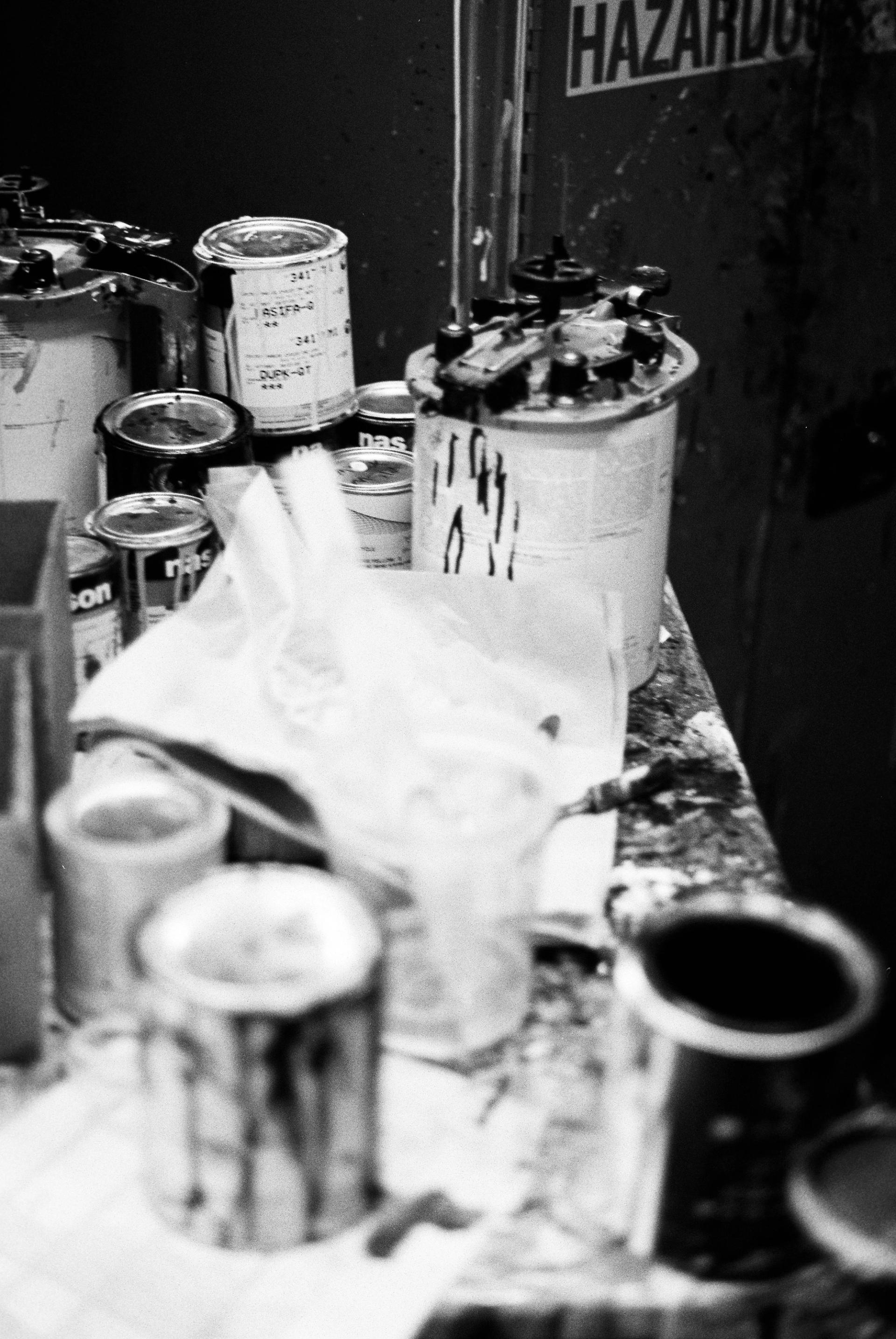 Black and white photograph of paint mixing equipment and canisters clustered together, their surfaces worn from years of use.