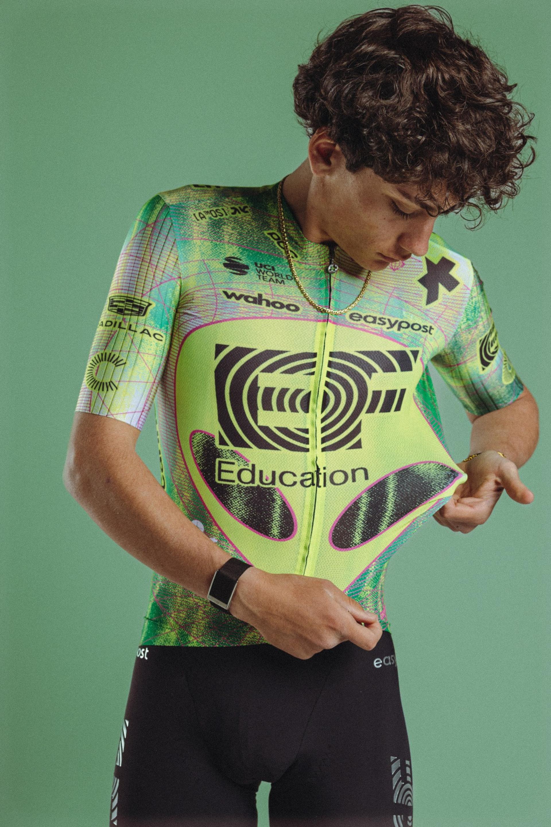 Cyclist in green team jersey celebrating with hands on hips against green backdrop
