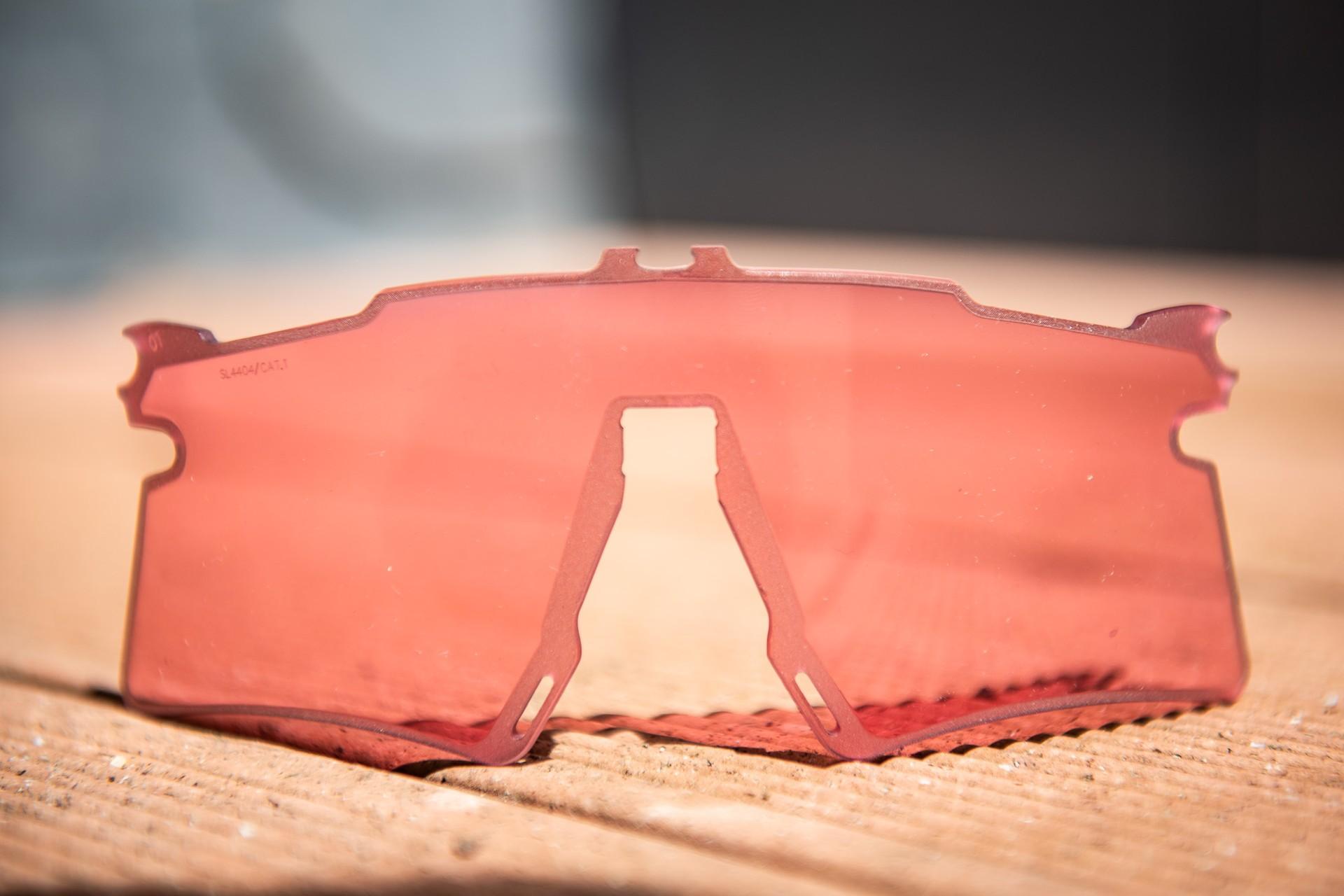 Red cycling sunglasses resting on a dusty surface, lens facing forward.