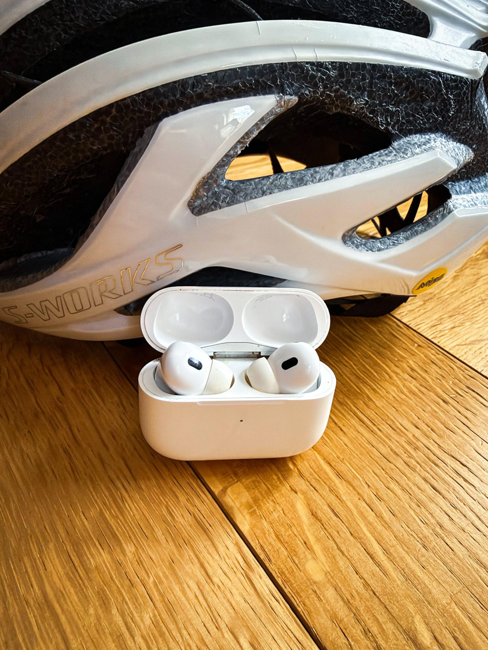 White wireless Apple Airpod earbuds in an open case beside a white Specialized S-Works cycling helmet