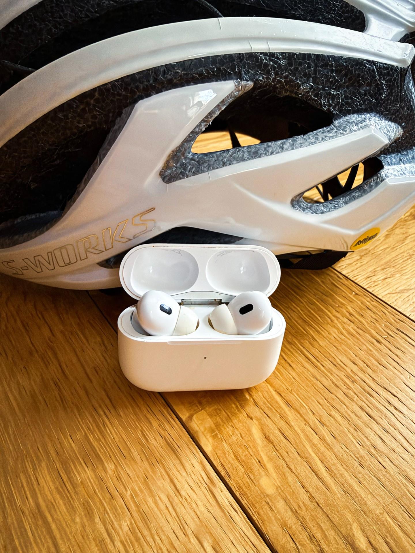 White wireless Apple Airpod earbuds in an open case beside a white Specialized S-Works cycling helmet