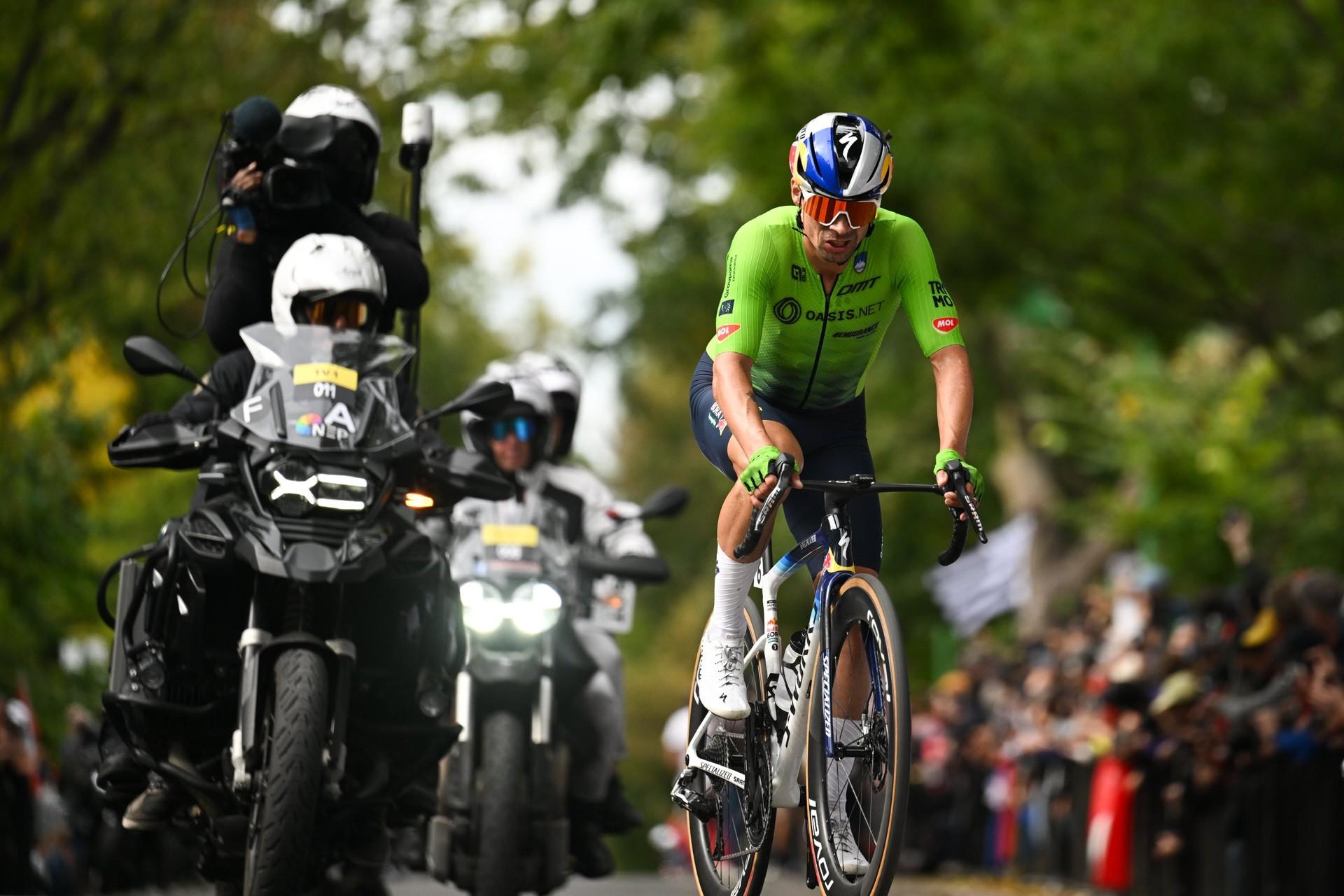 Cyclists ride along a road, with Remco Evenepoel in a green jersey leading the group.