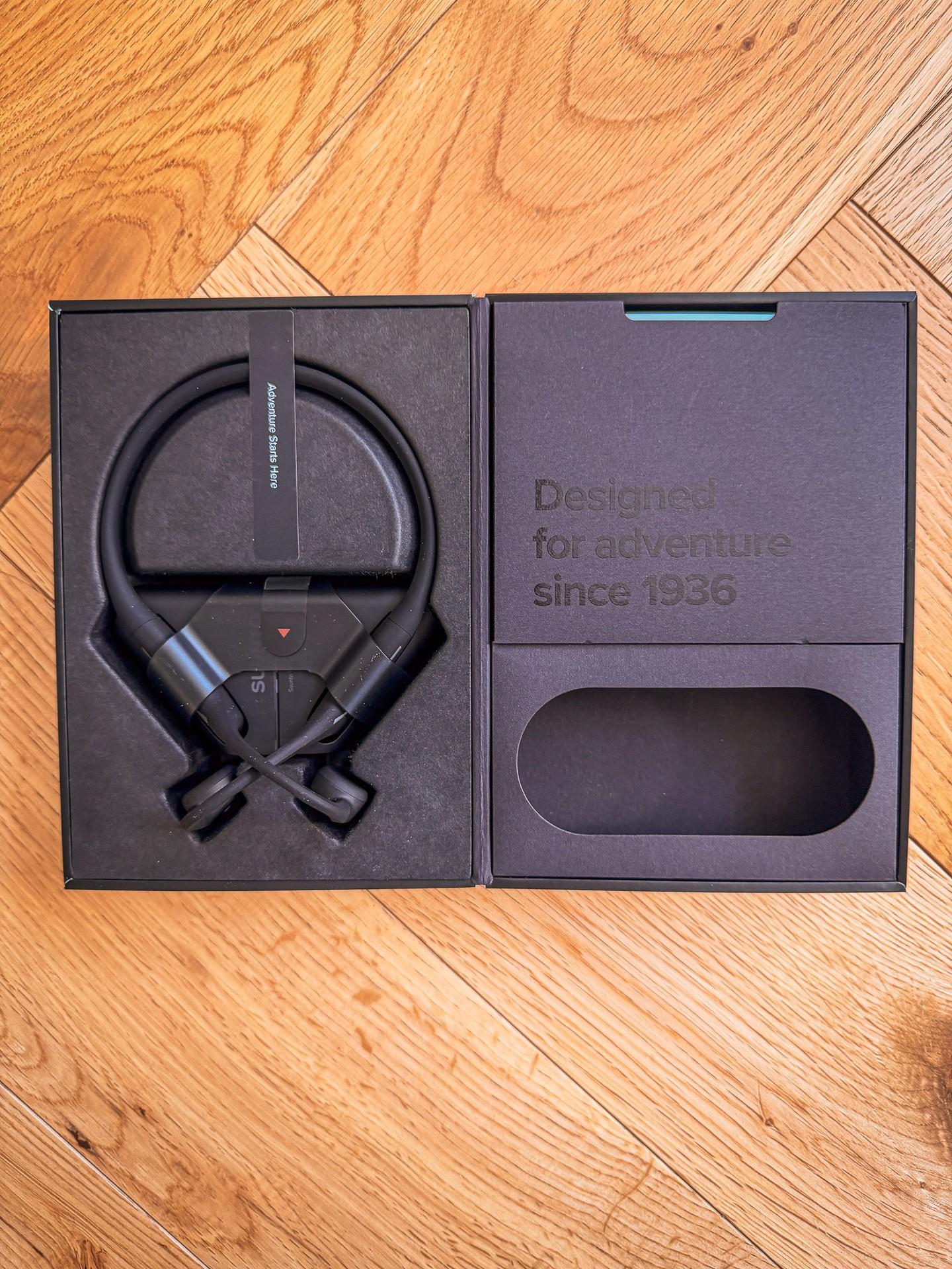 Suunto Wing 2 headphones and their powerbank shown in an open presentation case on a wooden surface.