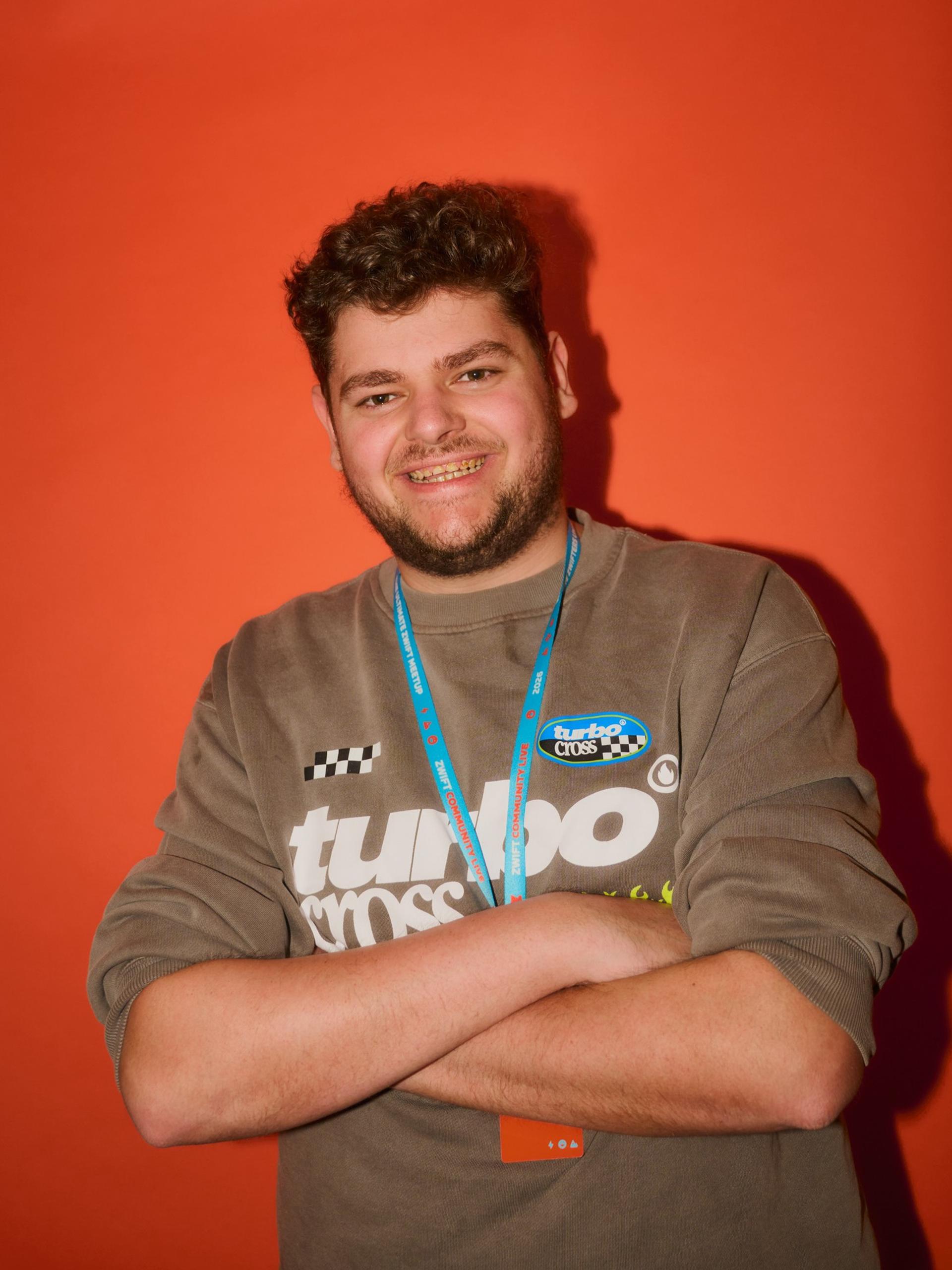 Smiling rider with a medal and lanyard, arms crossed, standing in front of an orange backdrop.