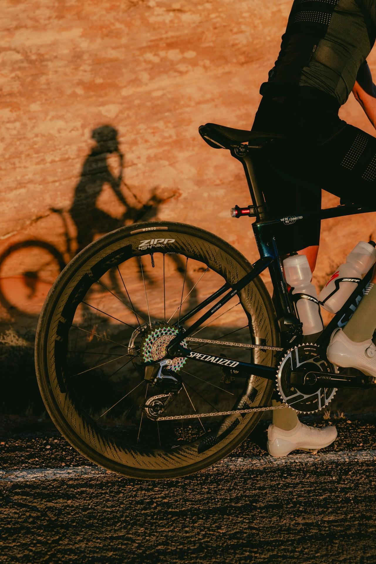 Cyclist in racing kit pedals a time-trial bike on a road at dusk.