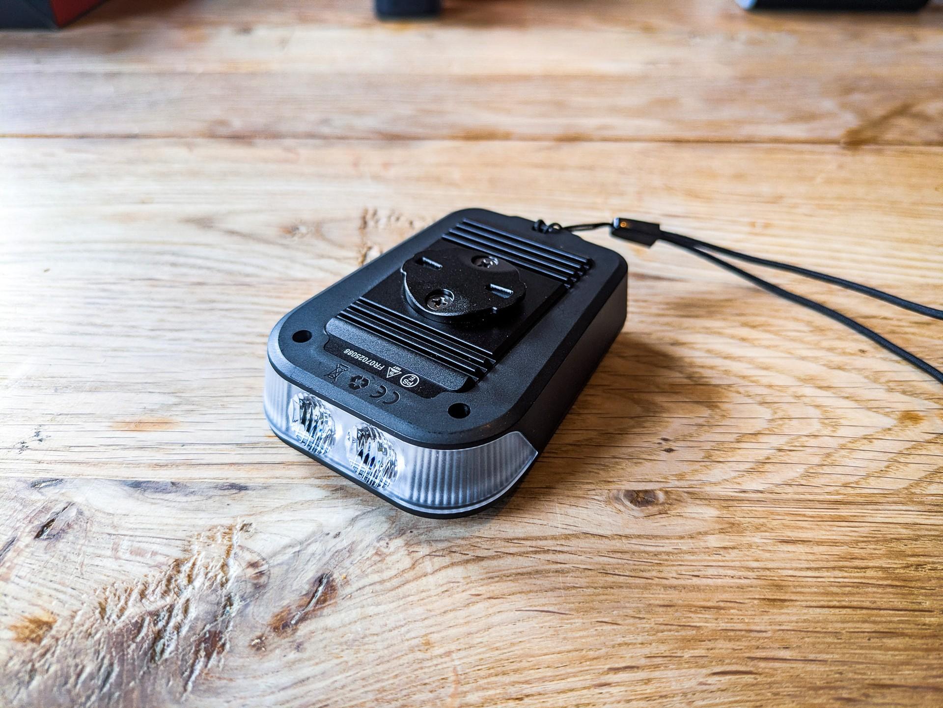 Ravemen FR 1100 SE front bike light on a wooden table, with its mount and cable visible.