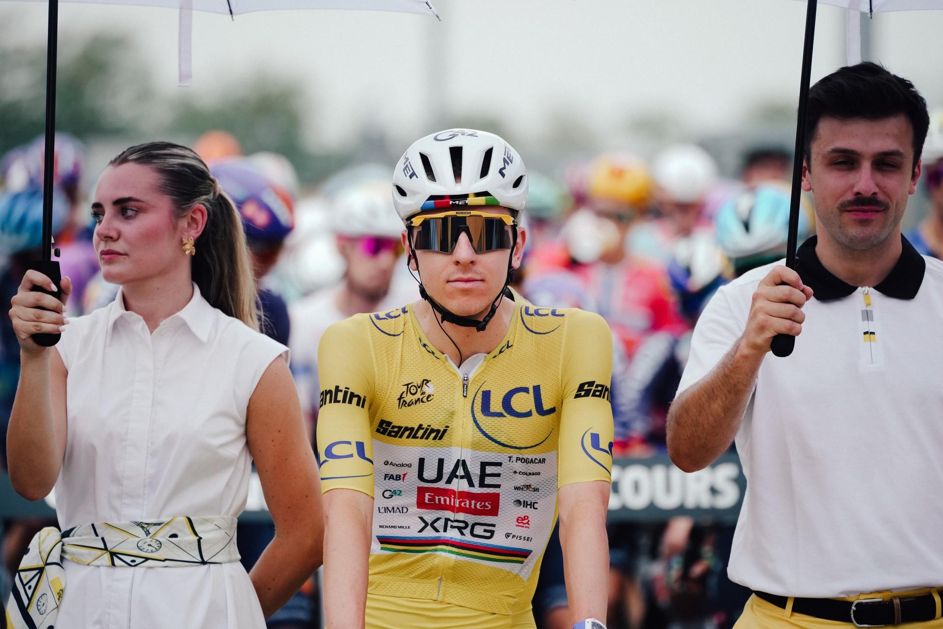 Tadej Pogačar in UAE Team Emirates kit ahead of the Tour de France stage, flanked by fans holding placards.