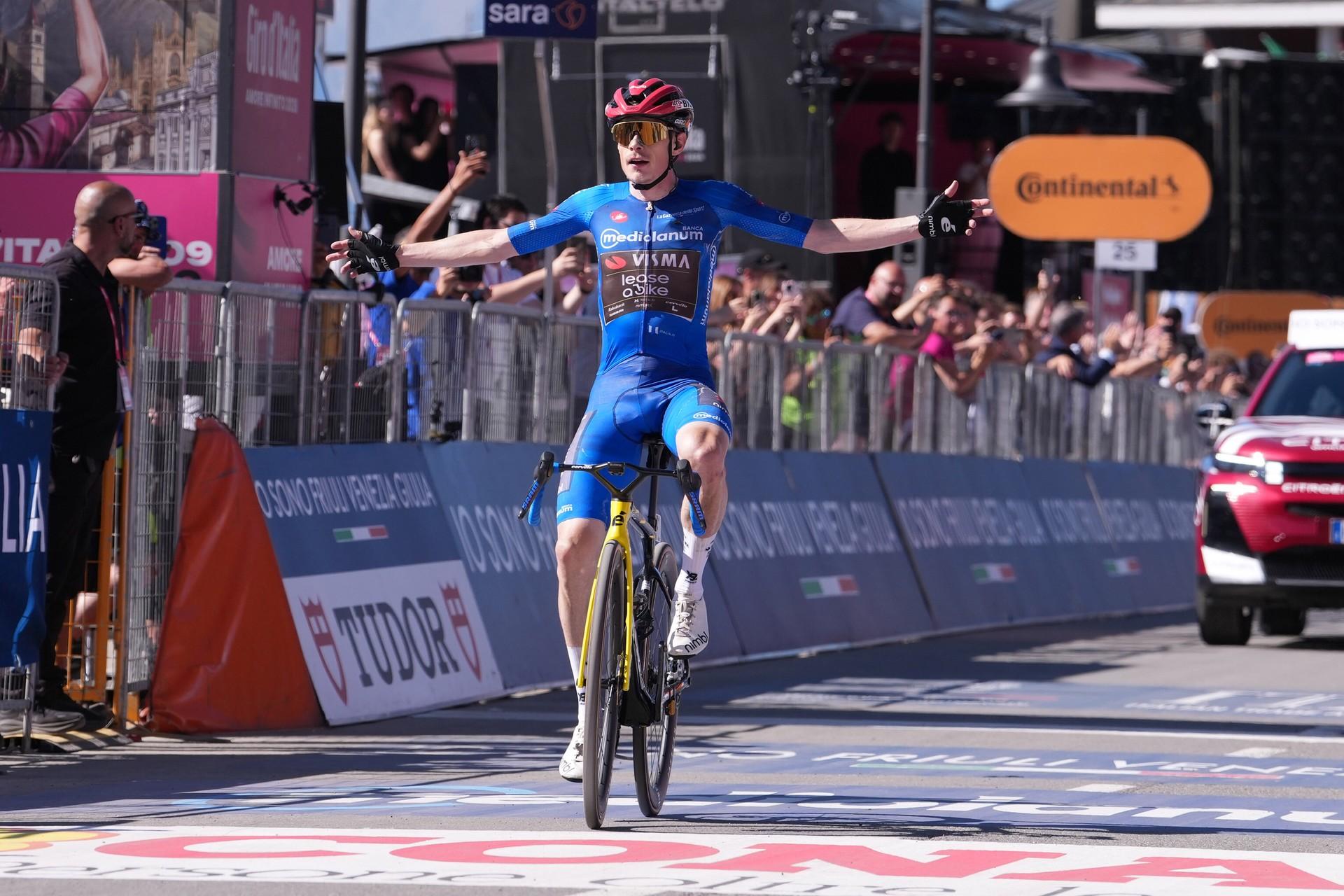 Cyclist in blue kit raises arms while sprinting to the finish line at a WorldTour stage race