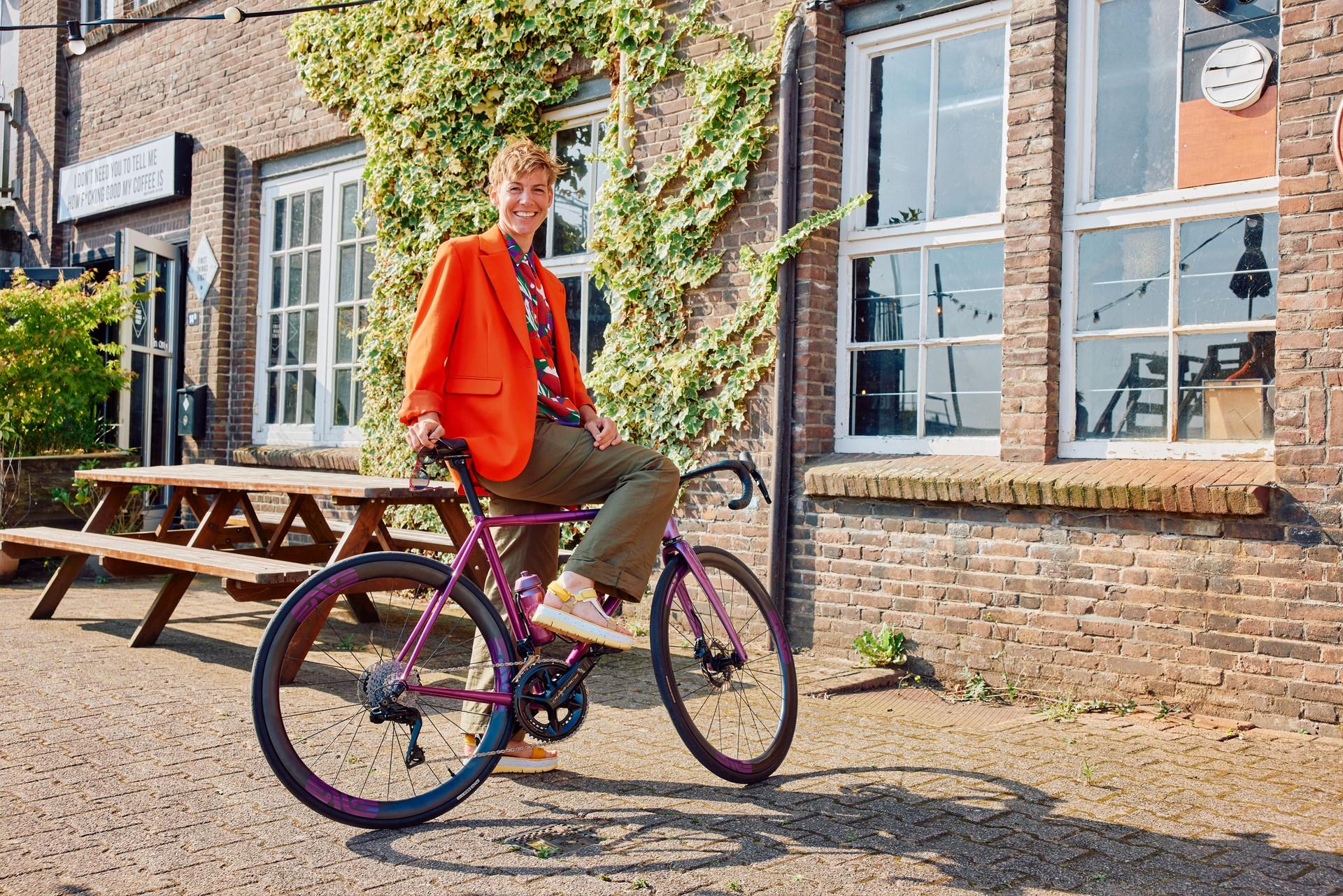 Cyclist in orange top rides a purple bike past a row of townhouses