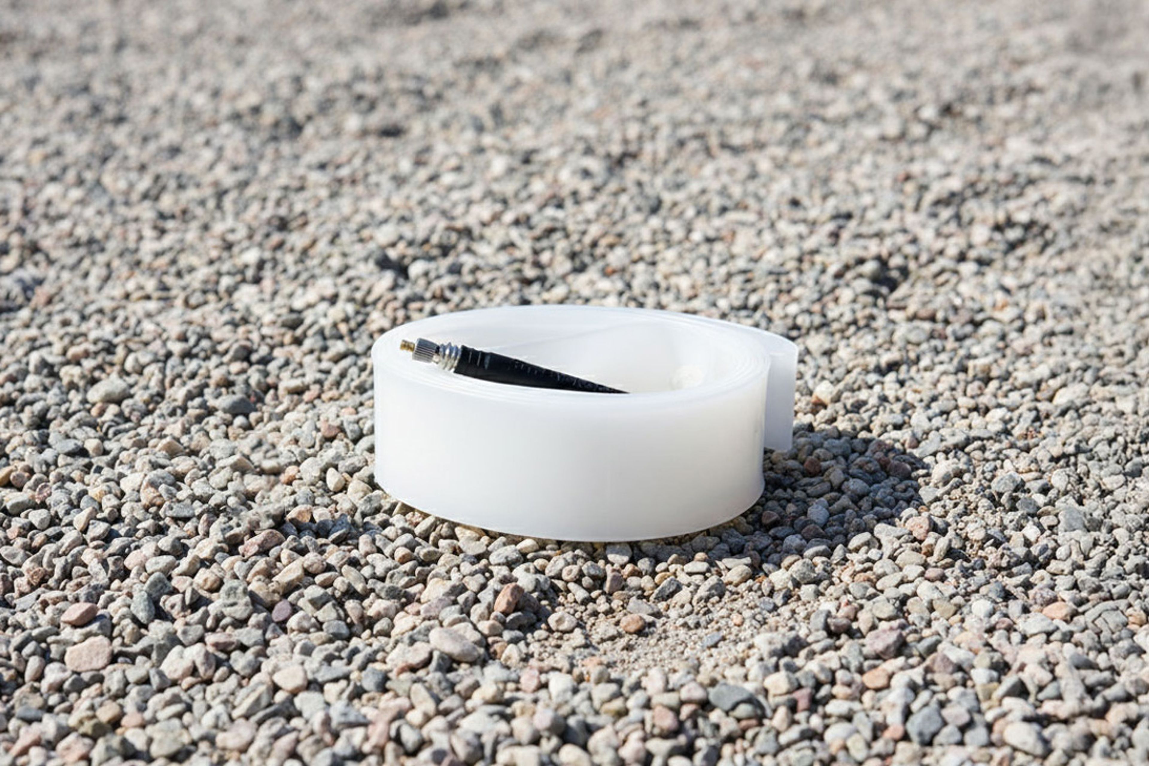 A Revoloop Ultra Race TPU inner tube sat flat on a gravel surface on a bright day
