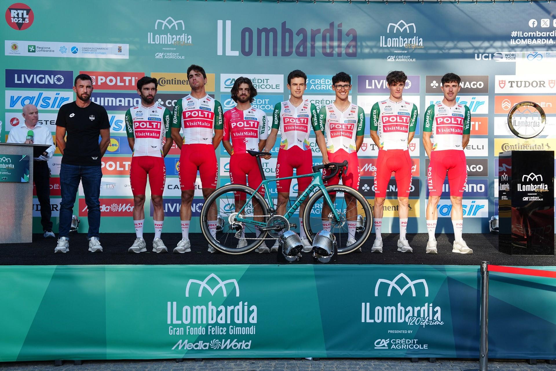 Professional cyclists pose with their bikes in front of an Il Lombardia sponsor backdrop.
