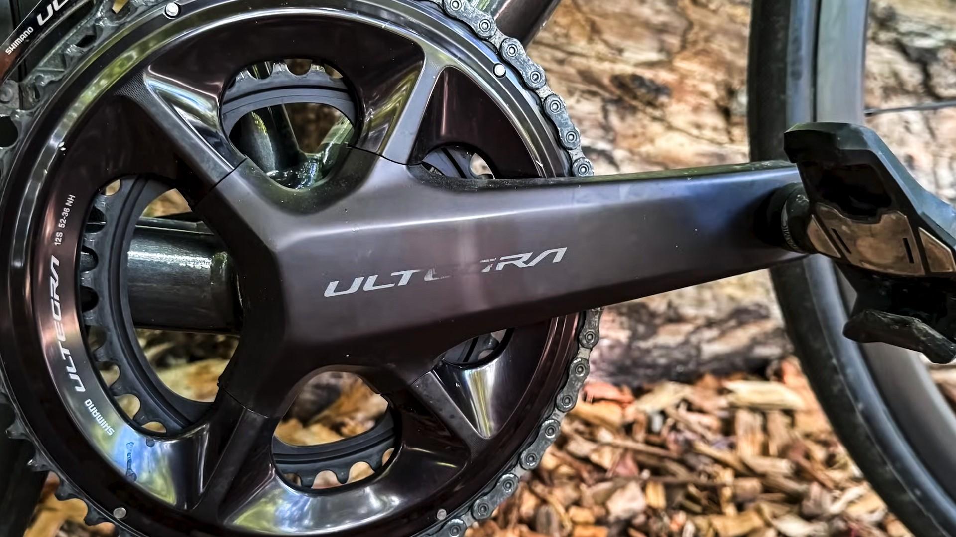 Close-up of a Shimano Ultegra road bike crankset and pedal against a natural wood background.