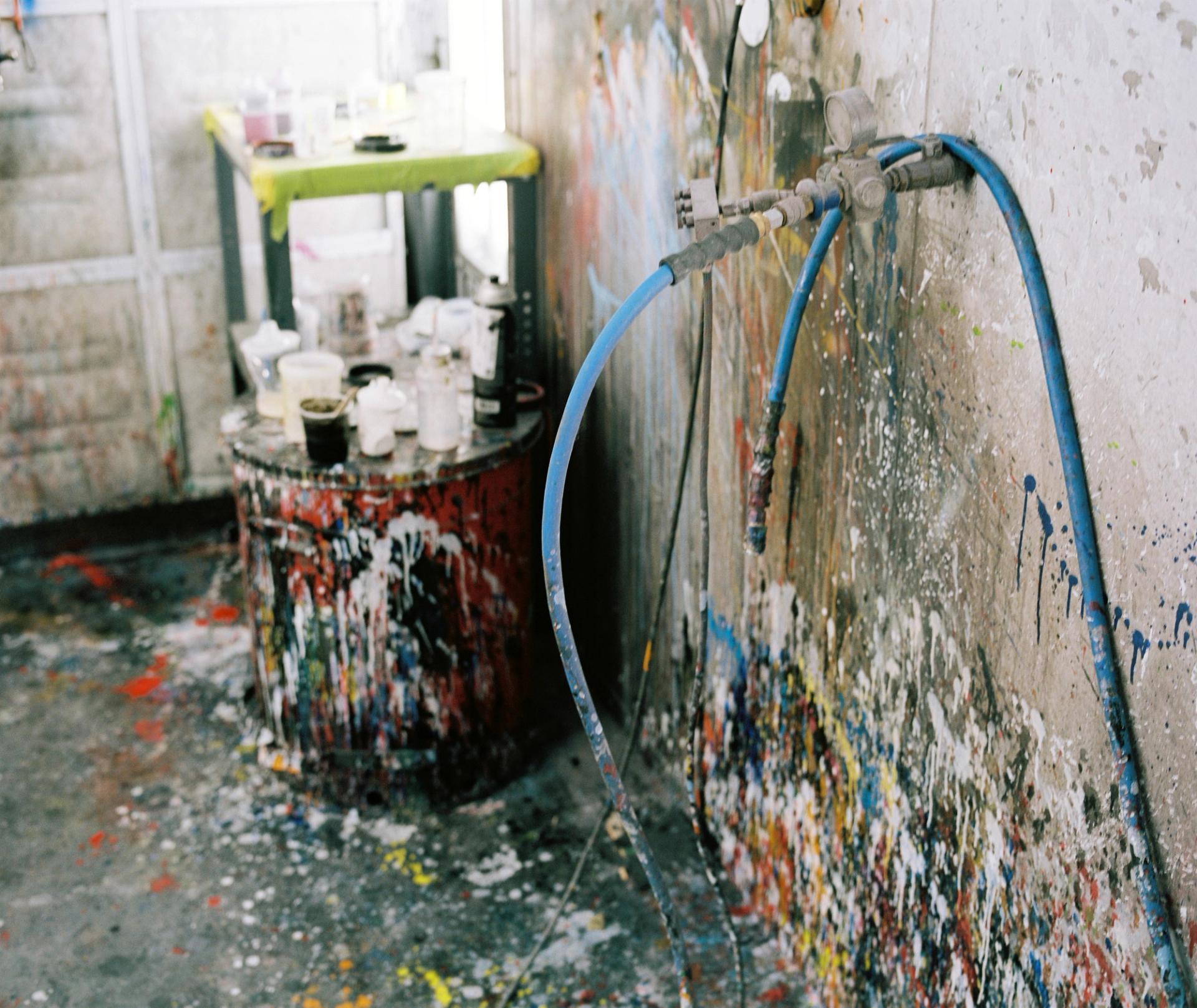 The interior of Parlee's paint booth showing years of accumulated overspray on walls and equipment, with spray lines and protective covers visible.