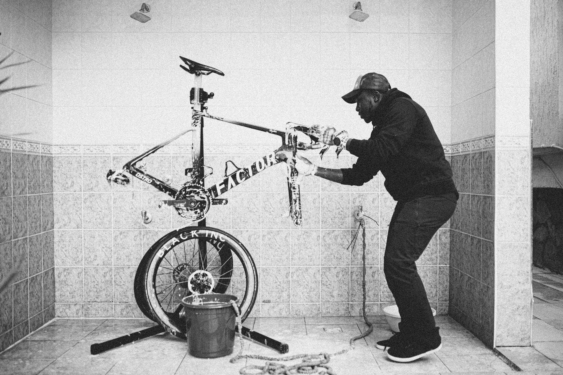 Cyclist wearing helmet adjusts a BMX-style track bike while working on training equipment indoors